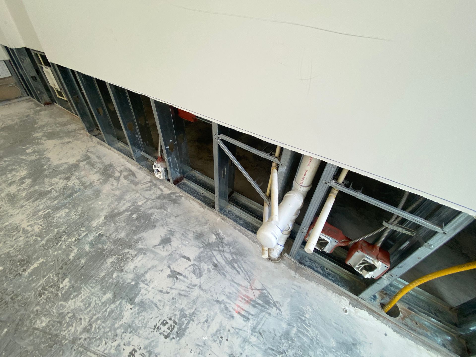 Construction site interior; exposed metal studs, pipes, and wiring along wall base.
