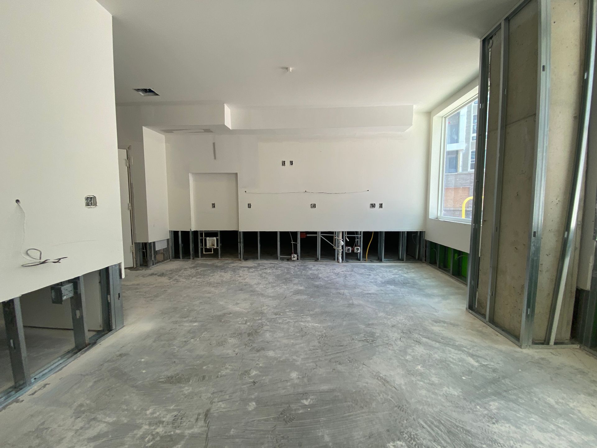 Interior room under construction, featuring exposed studs, unfinished drywall, and concrete floor.