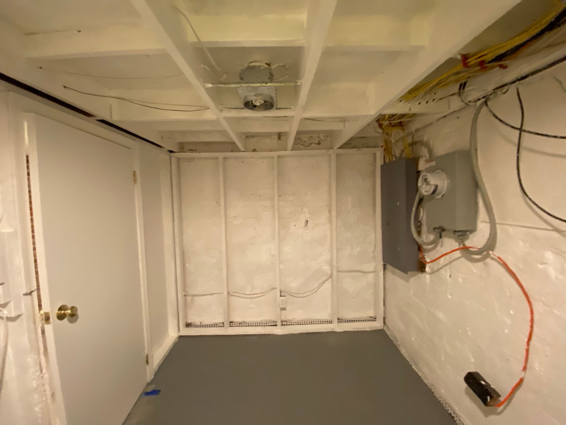 Basement interior with exposed studs, white painted walls and ceiling, gray floor, electrical panel.