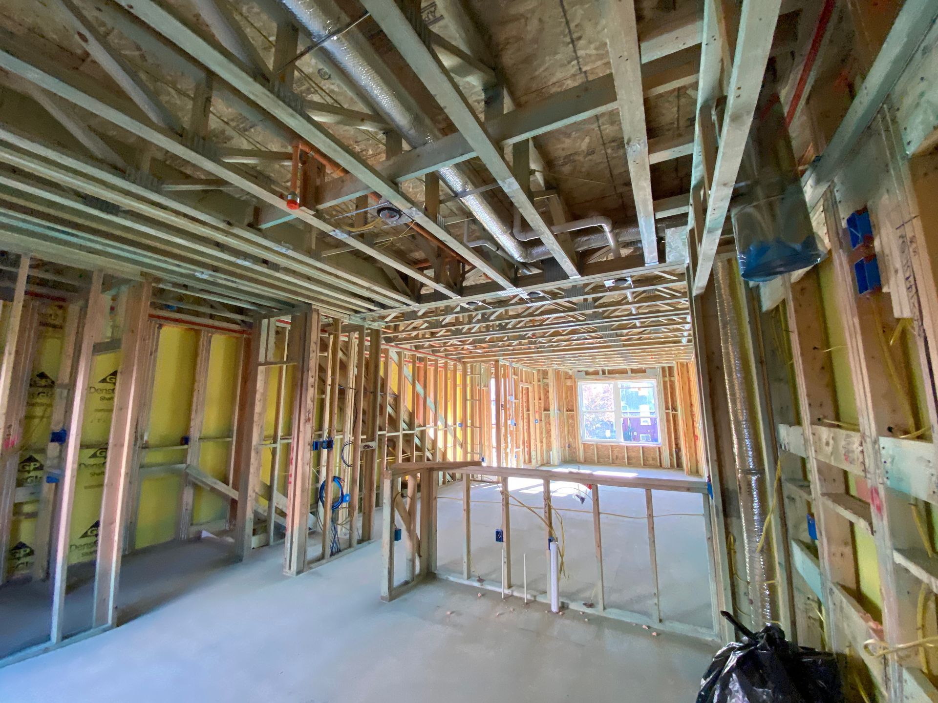 Interior framing of a building under construction, showing wooden studs, insulation, pipes, and wiring.