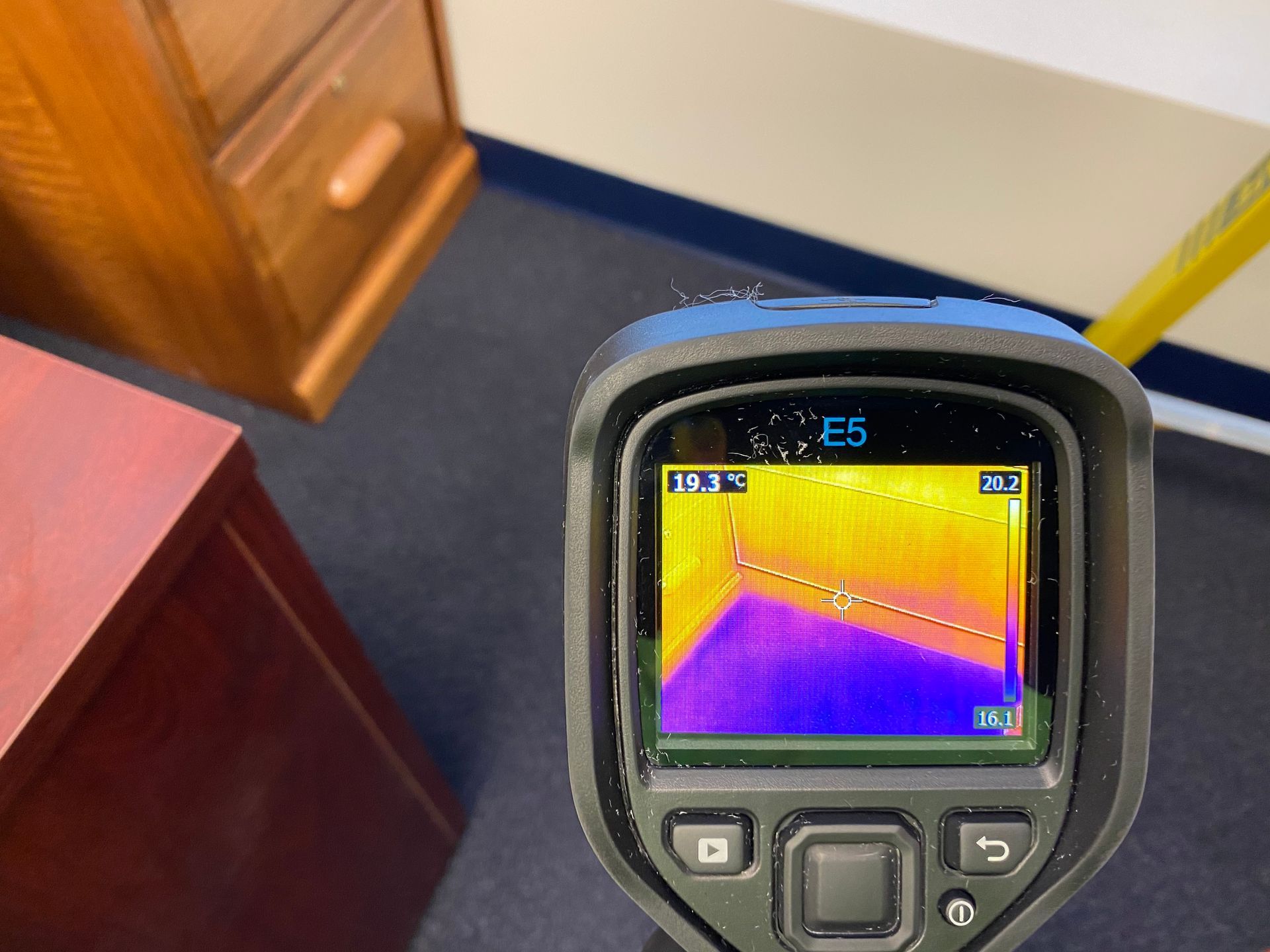 Thermal camera displaying a color map of a room corner; cooler blue and purple areas and warmer orange and yellow areas.