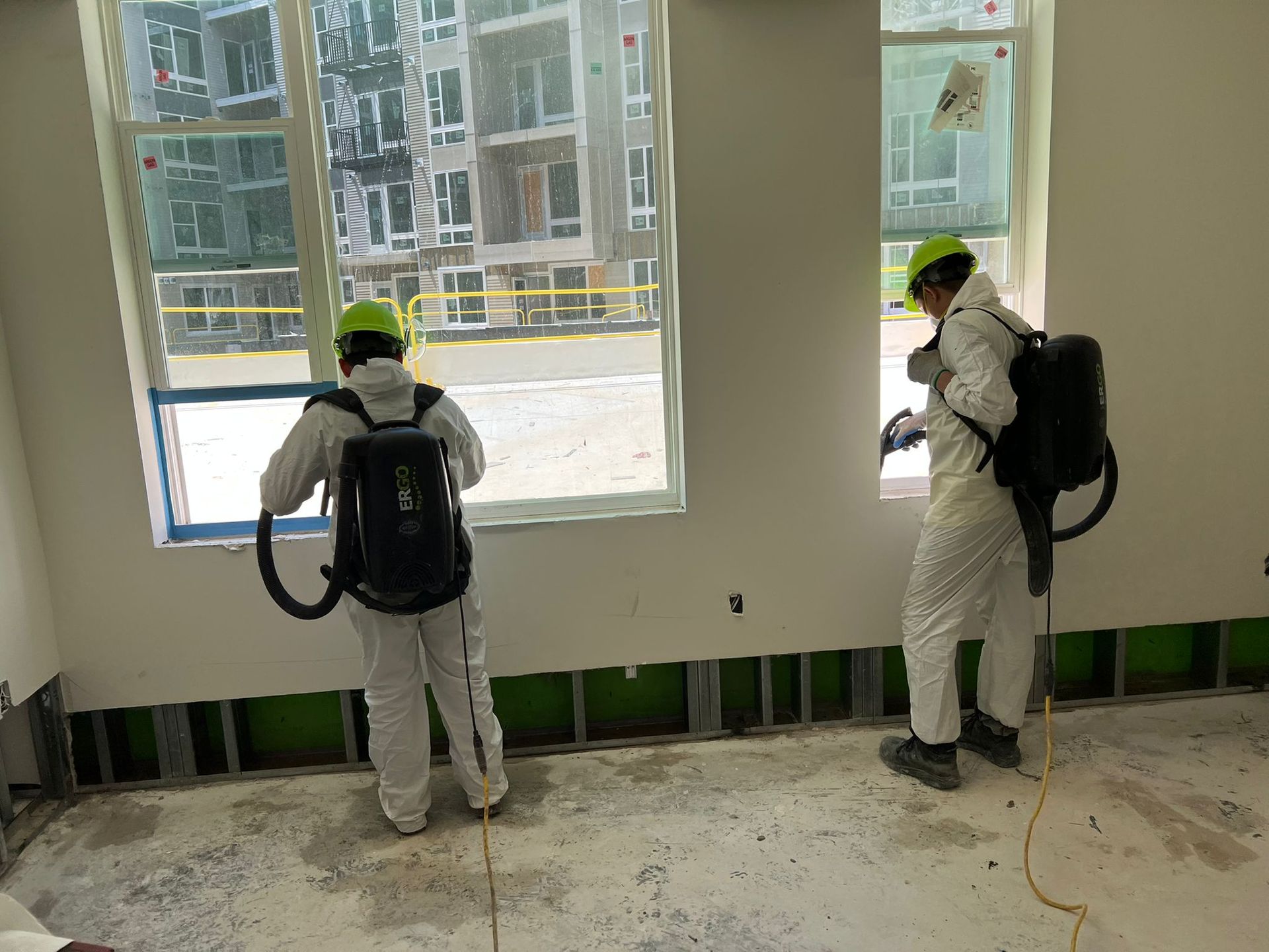 Two workers in protective suits spraying inside a building under construction.