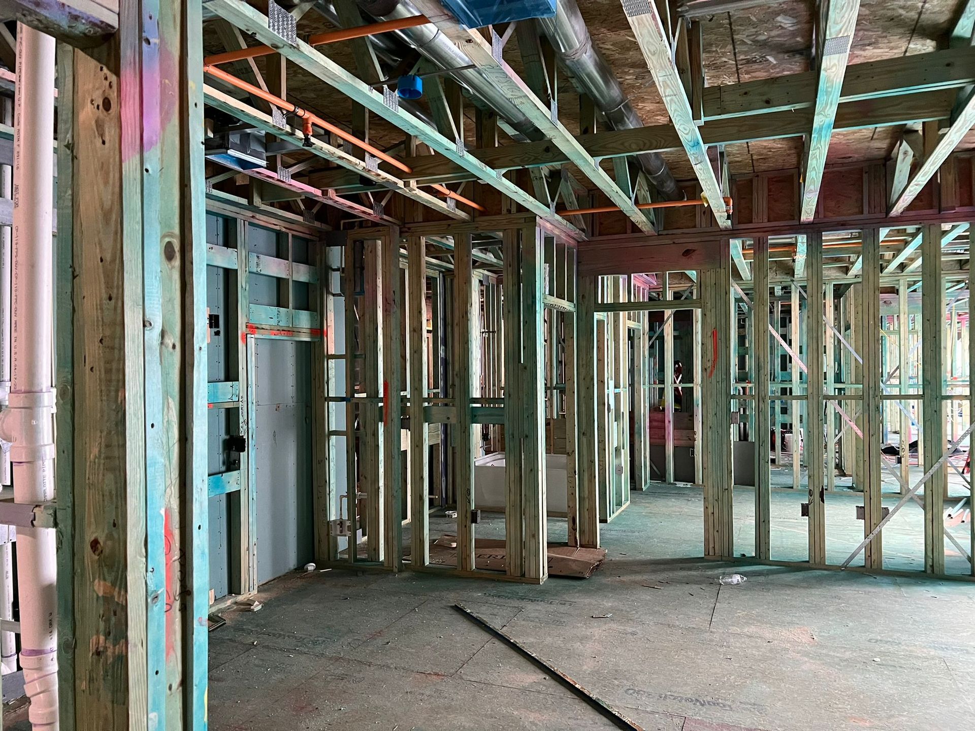 Interior view of a building under construction, showing wooden framing, pipes, and unfinished surfaces.
