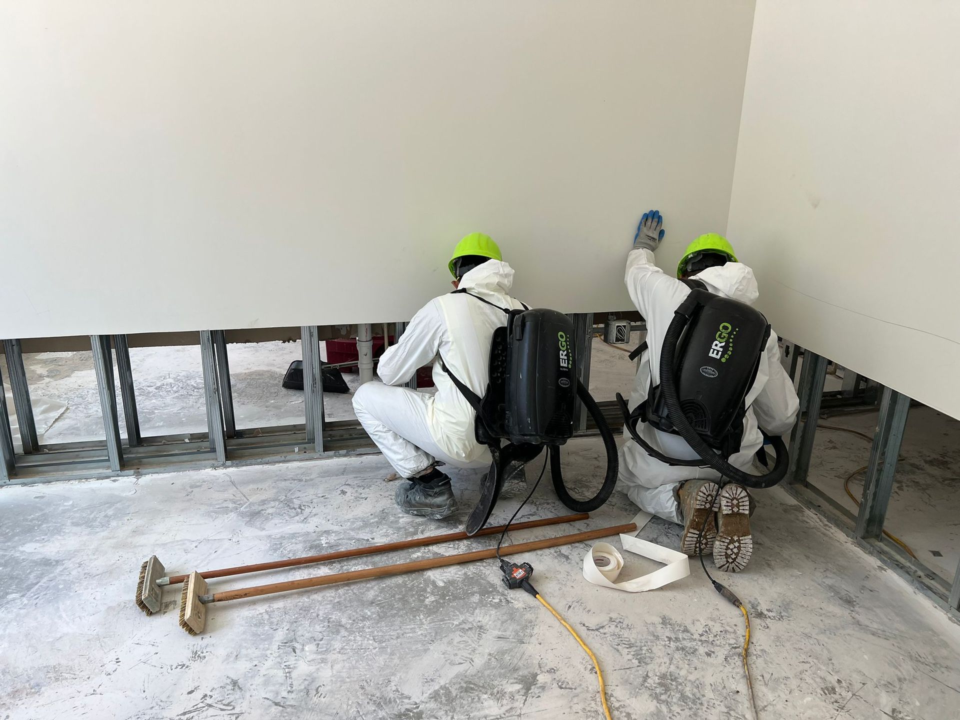 Two workers in protective suits spraying a wall, construction site.