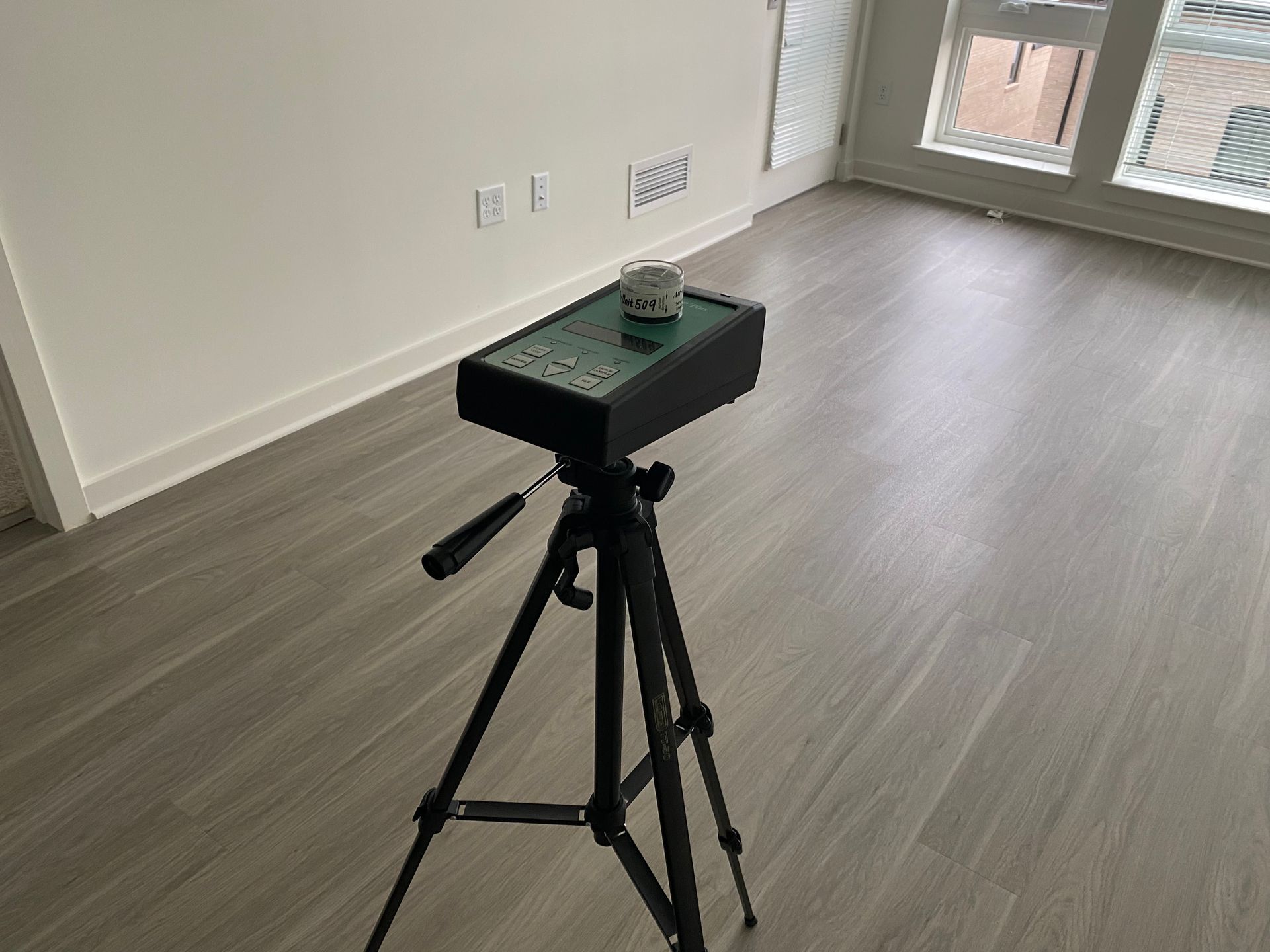 Tripod with a black device in an empty room, possibly for scanning.