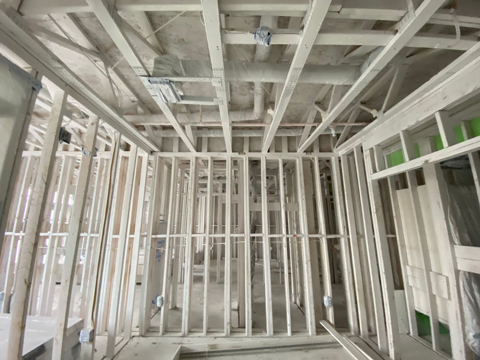 Interior wooden framing of a building under construction, showing walls, ceiling supports, and electrical wiring.