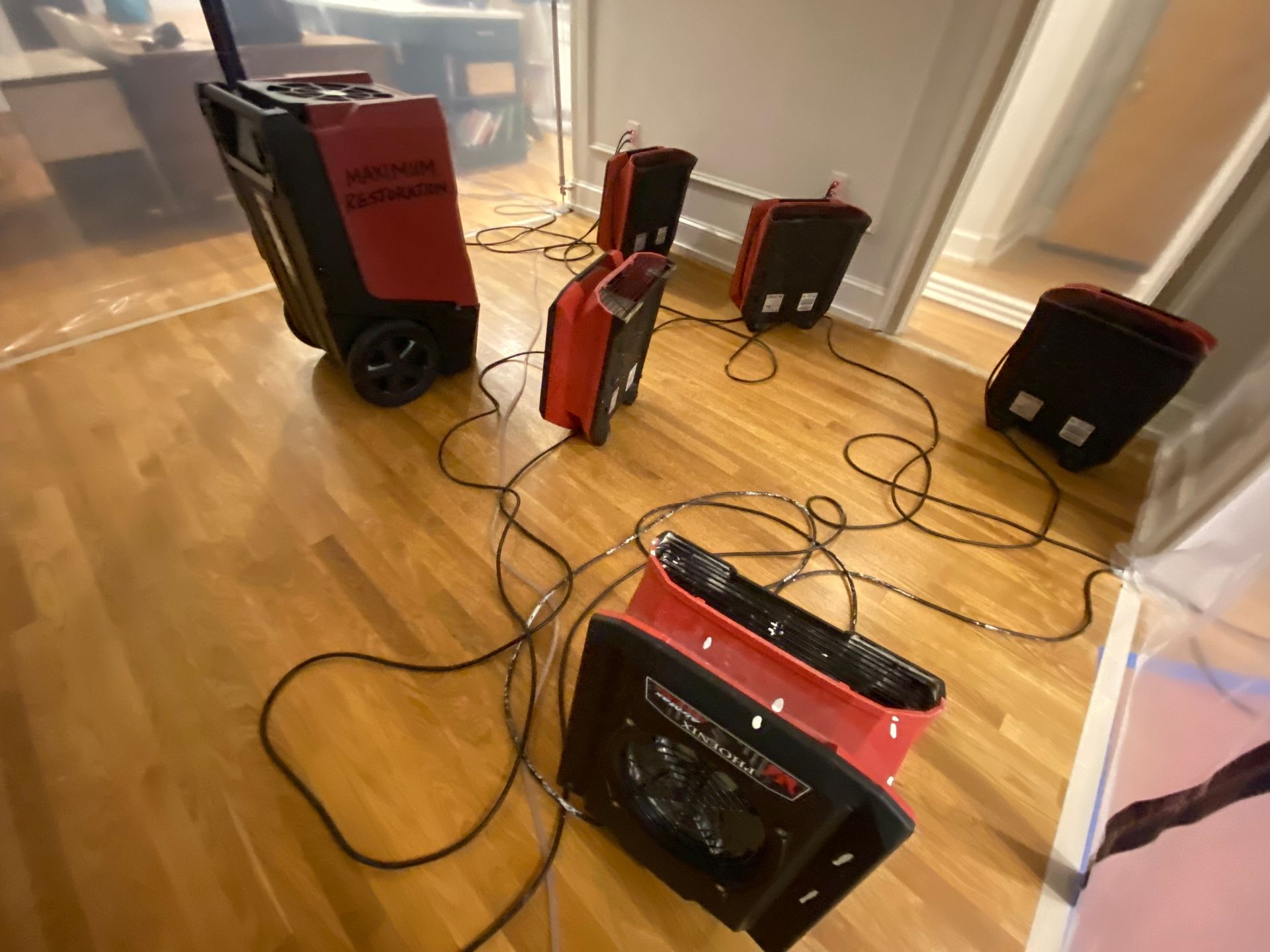 Dehumidifiers drying a room with wood flooring. Some are red and black, with cords running across the floor.