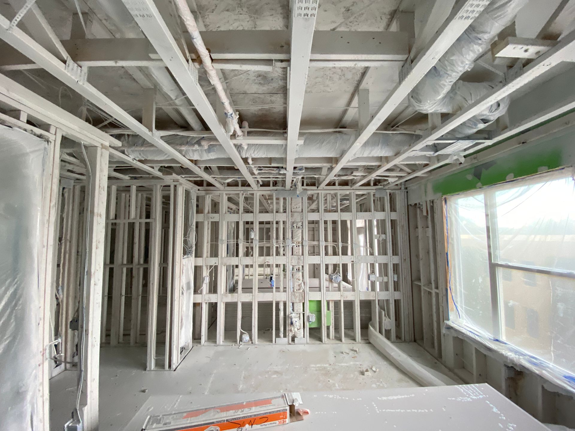 Interior framing of a room under construction with exposed beams, pipes, and a window.