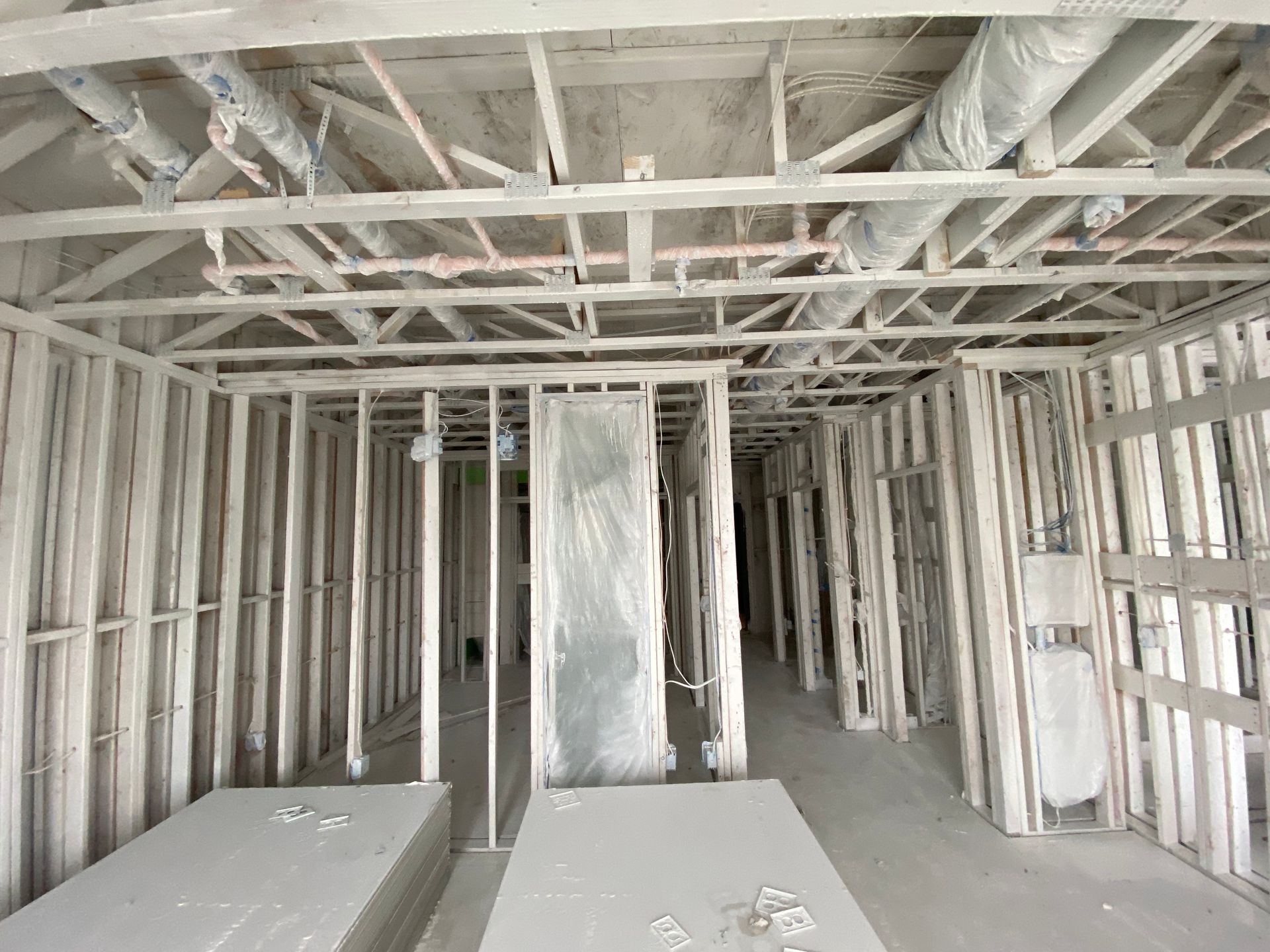 Interior view of a construction site with exposed wooden framing and ductwork, covered in white dust.
