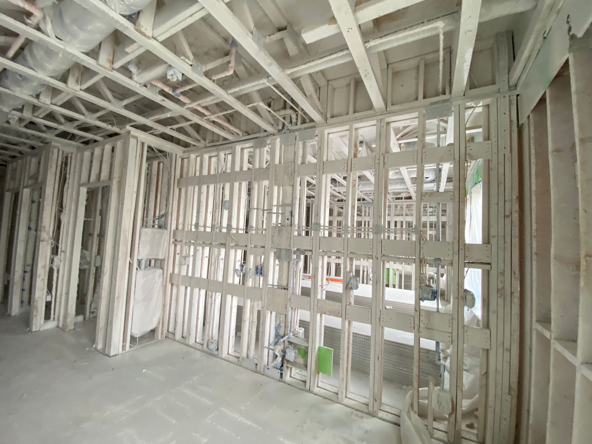 Interior of a building under construction, showing exposed wooden framing, pipes, and electrical wiring.