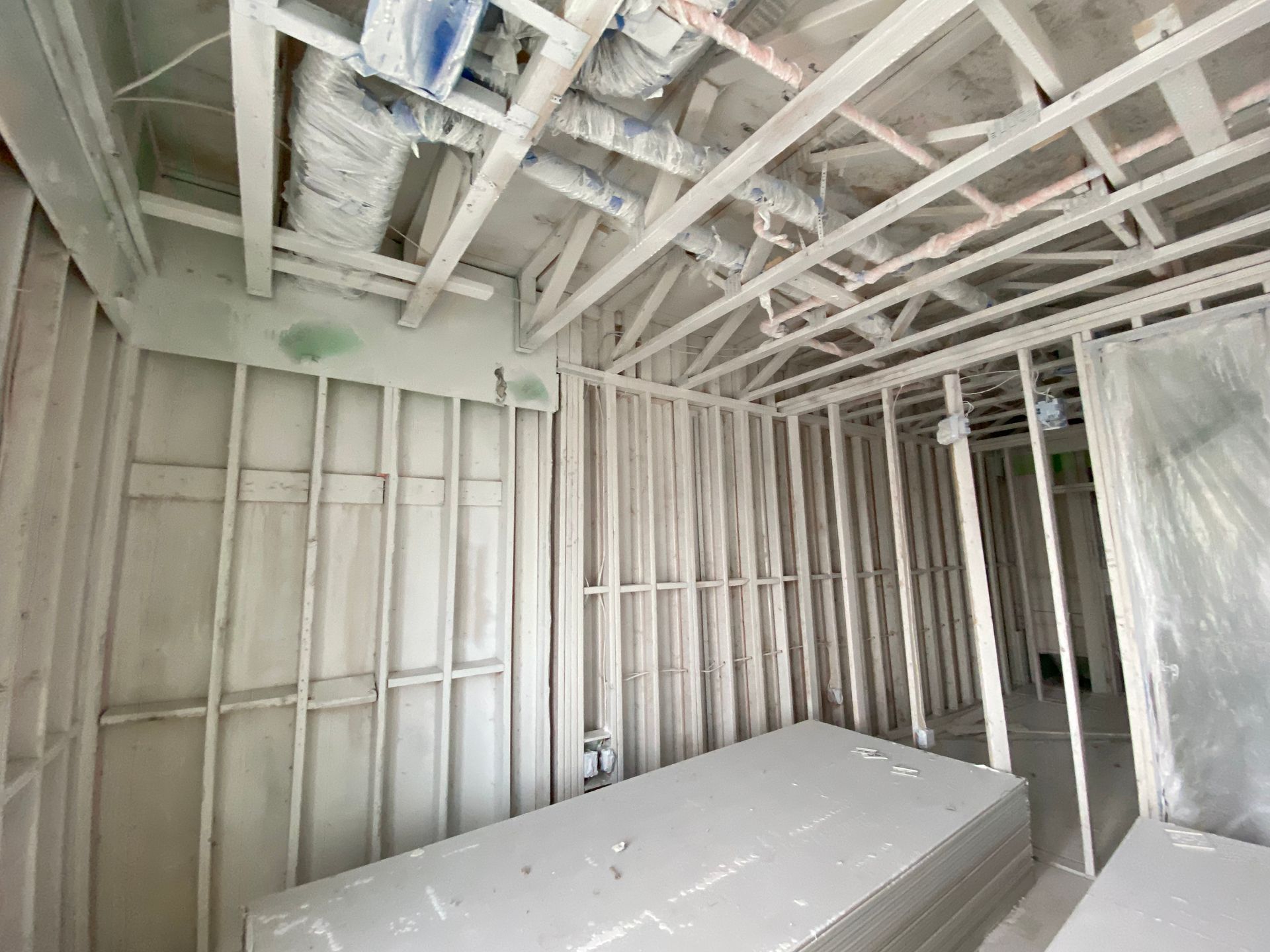 Interior of a room under construction, with wooden studs, drywall, and exposed ceiling beams.