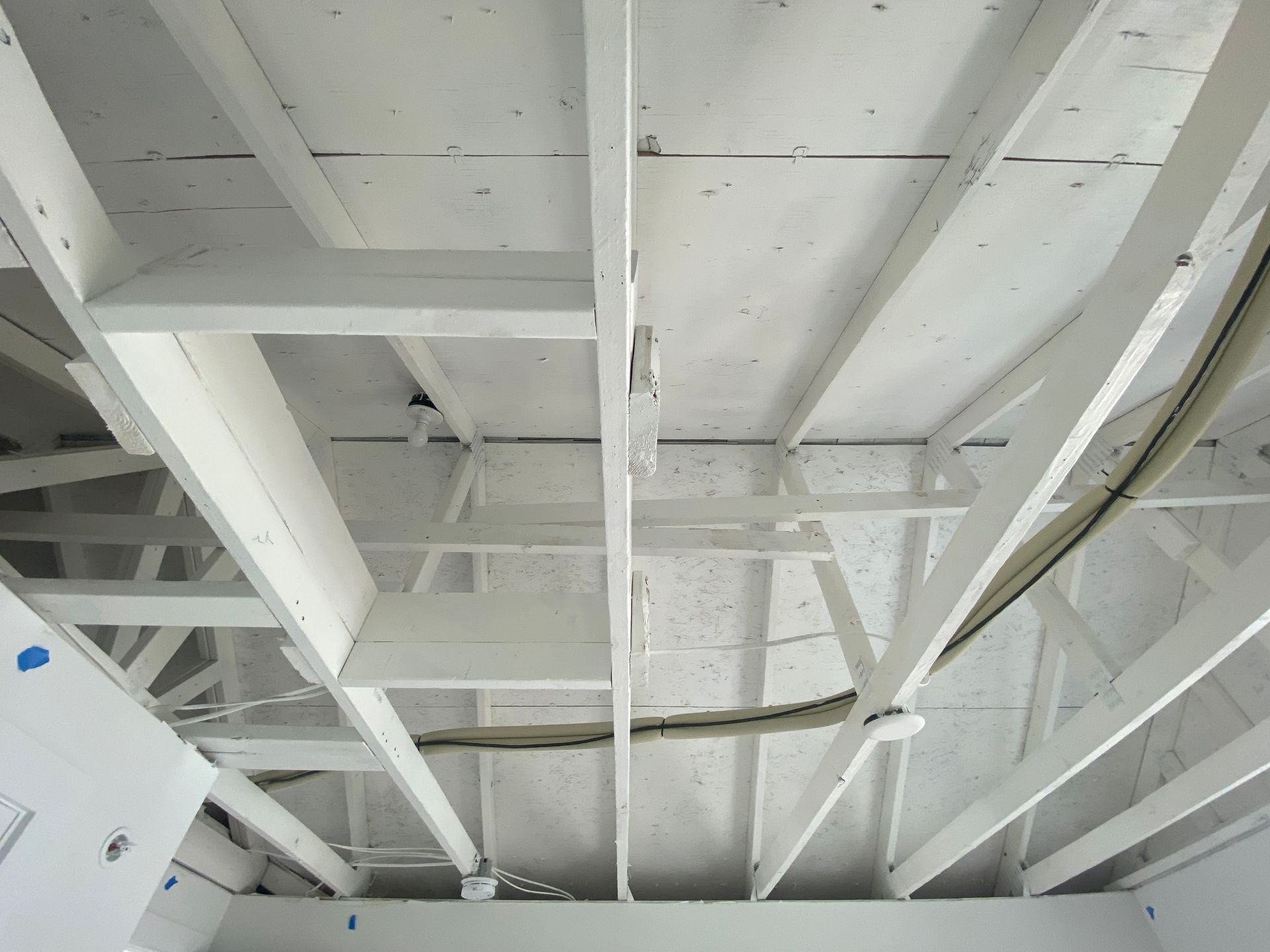 White-painted wooden ceiling framework with trusses and electrical wiring visible.