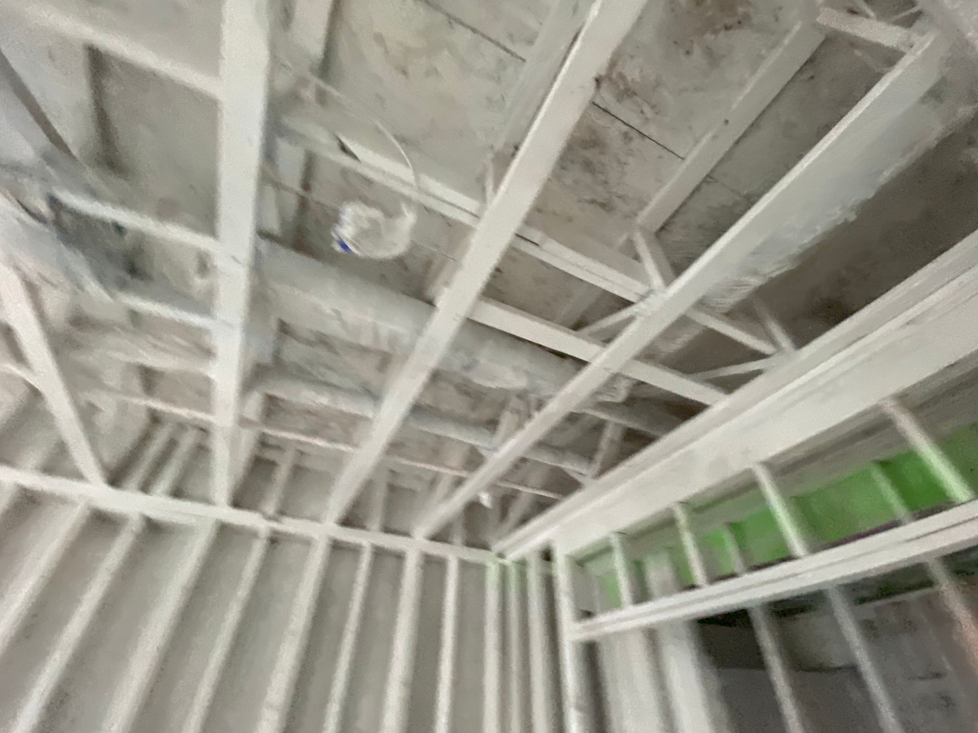 Interior view of a building's unfinished ceiling and wall framing, painted white.