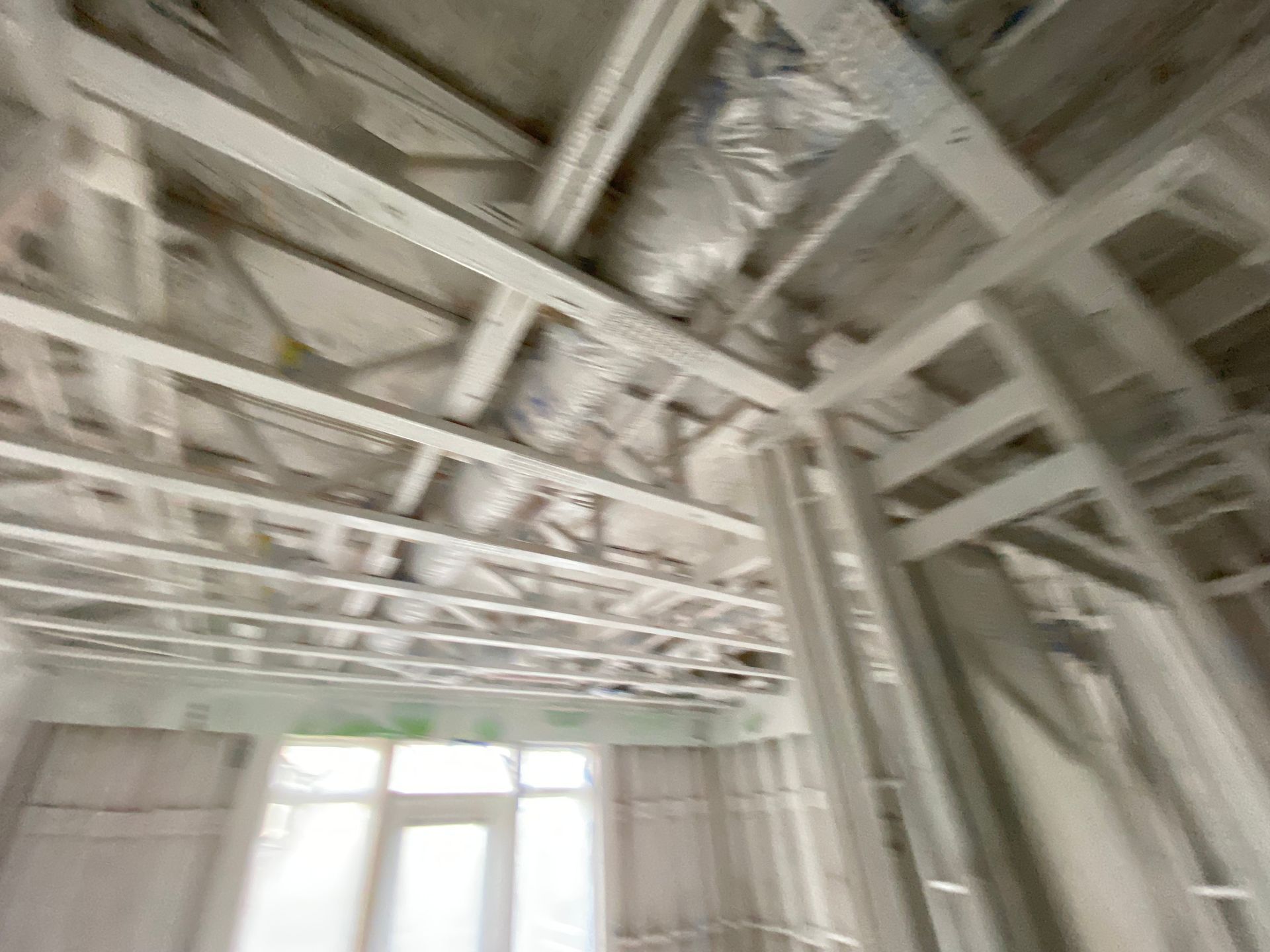 Interior view of a building under construction, showing framing, ceiling beams, and a window.