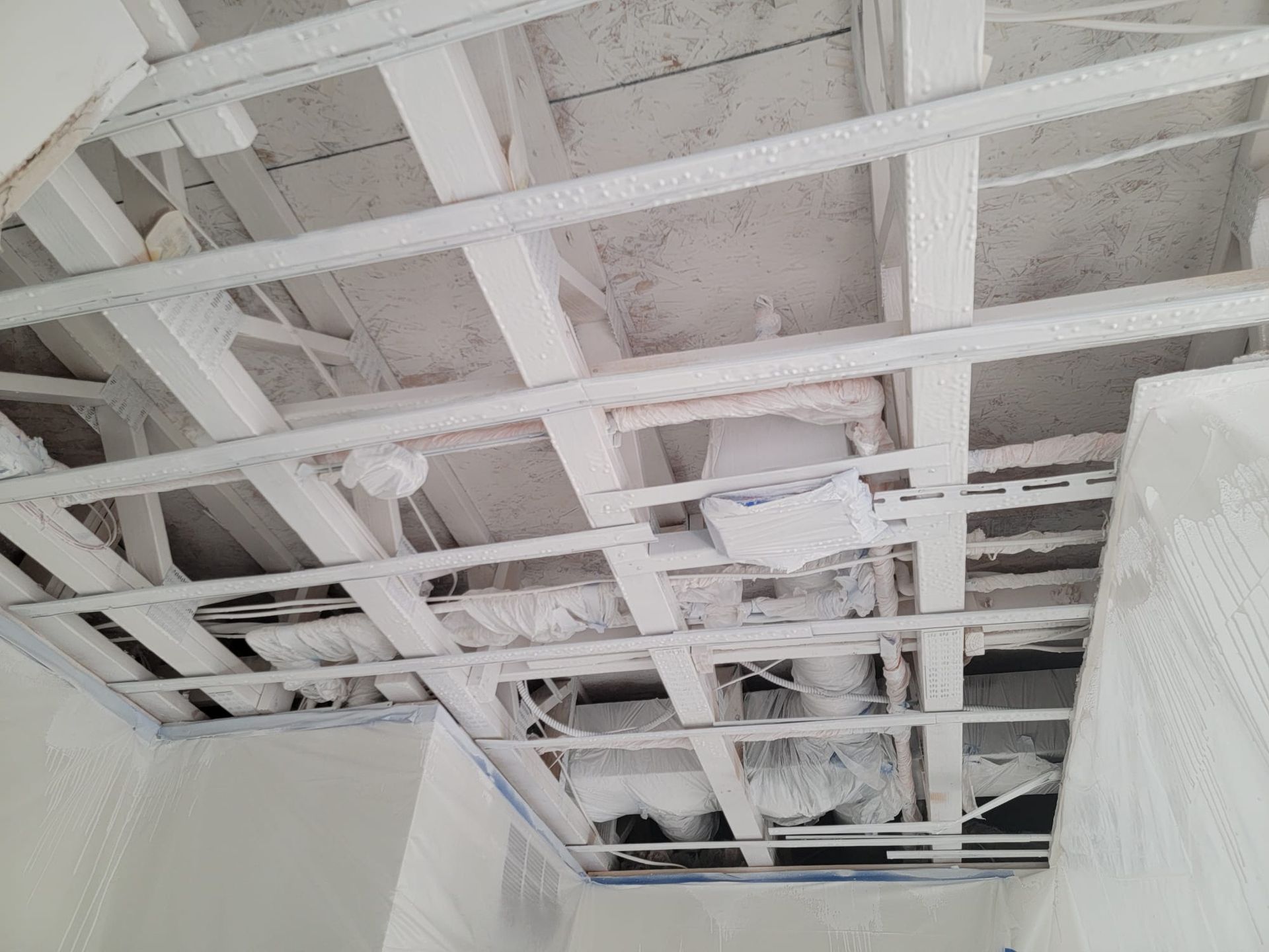 White ceiling grid with exposed ductwork and electrical wiring.