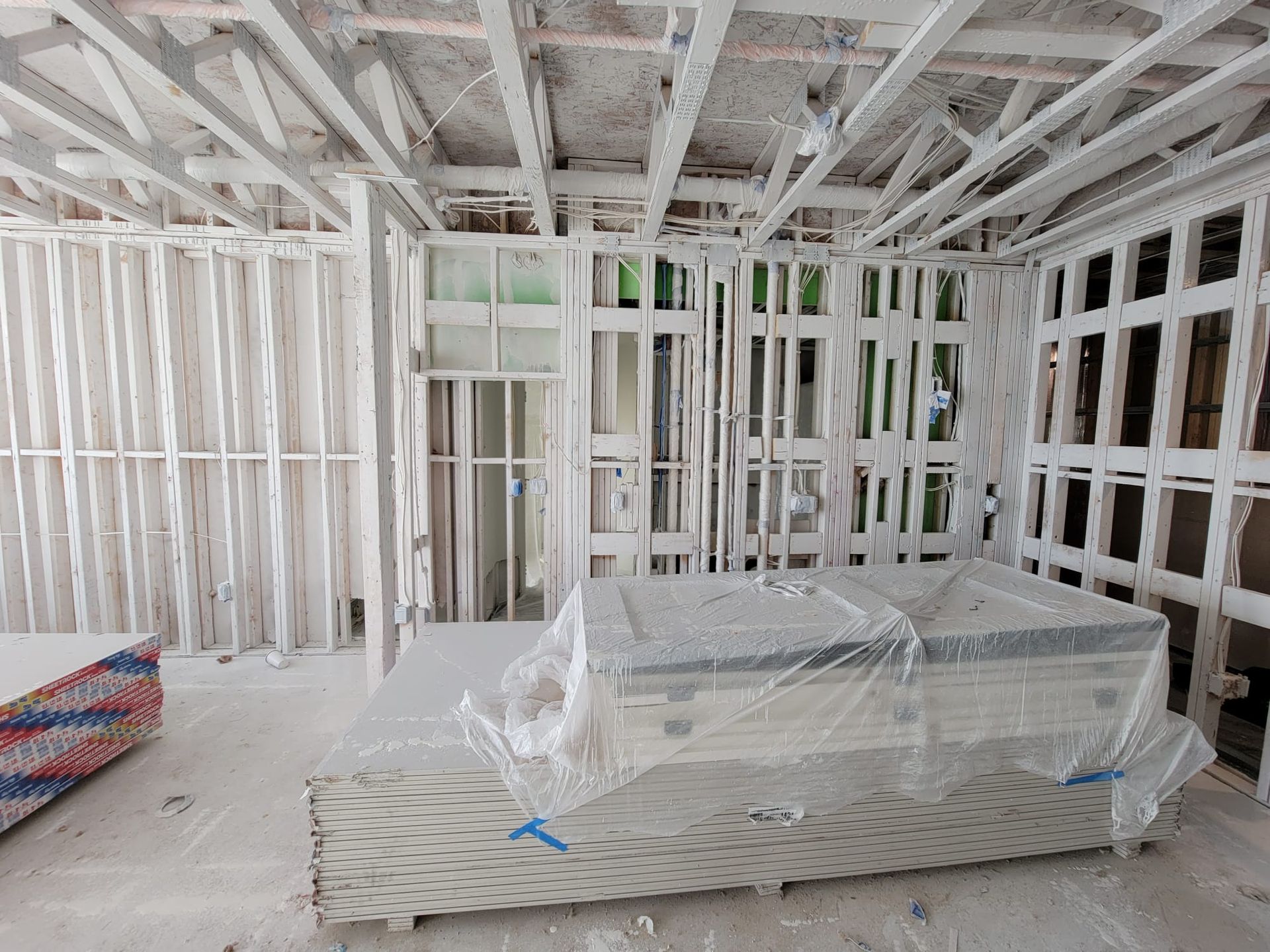 Interior view of a room under construction with white framing, drywall, and a covered item in the center.