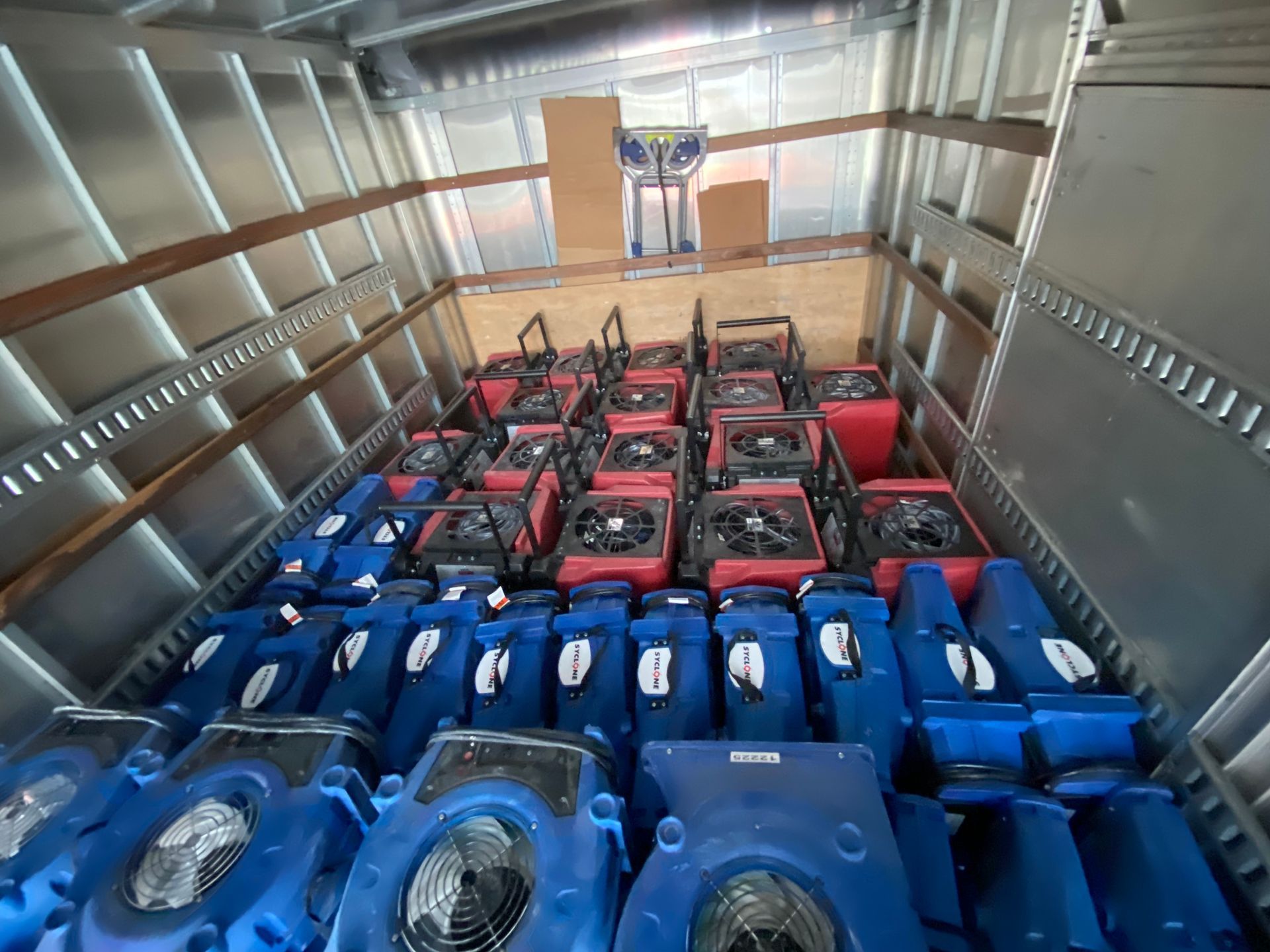 A truck interior filled with rows of blue and red air movers and fans, possibly for water damage restoration.