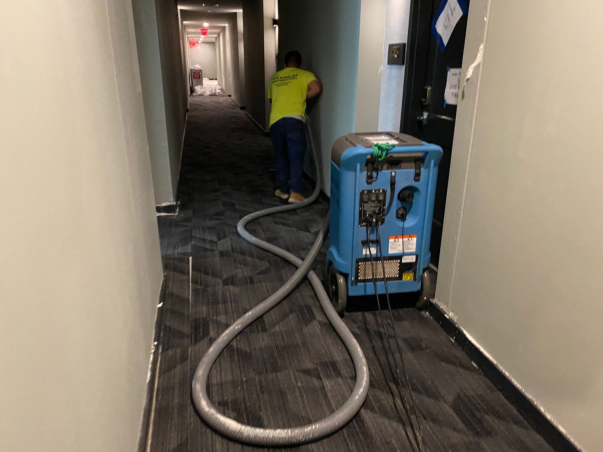 Man using a water extraction machine in a hallway with damaged walls and flooring.