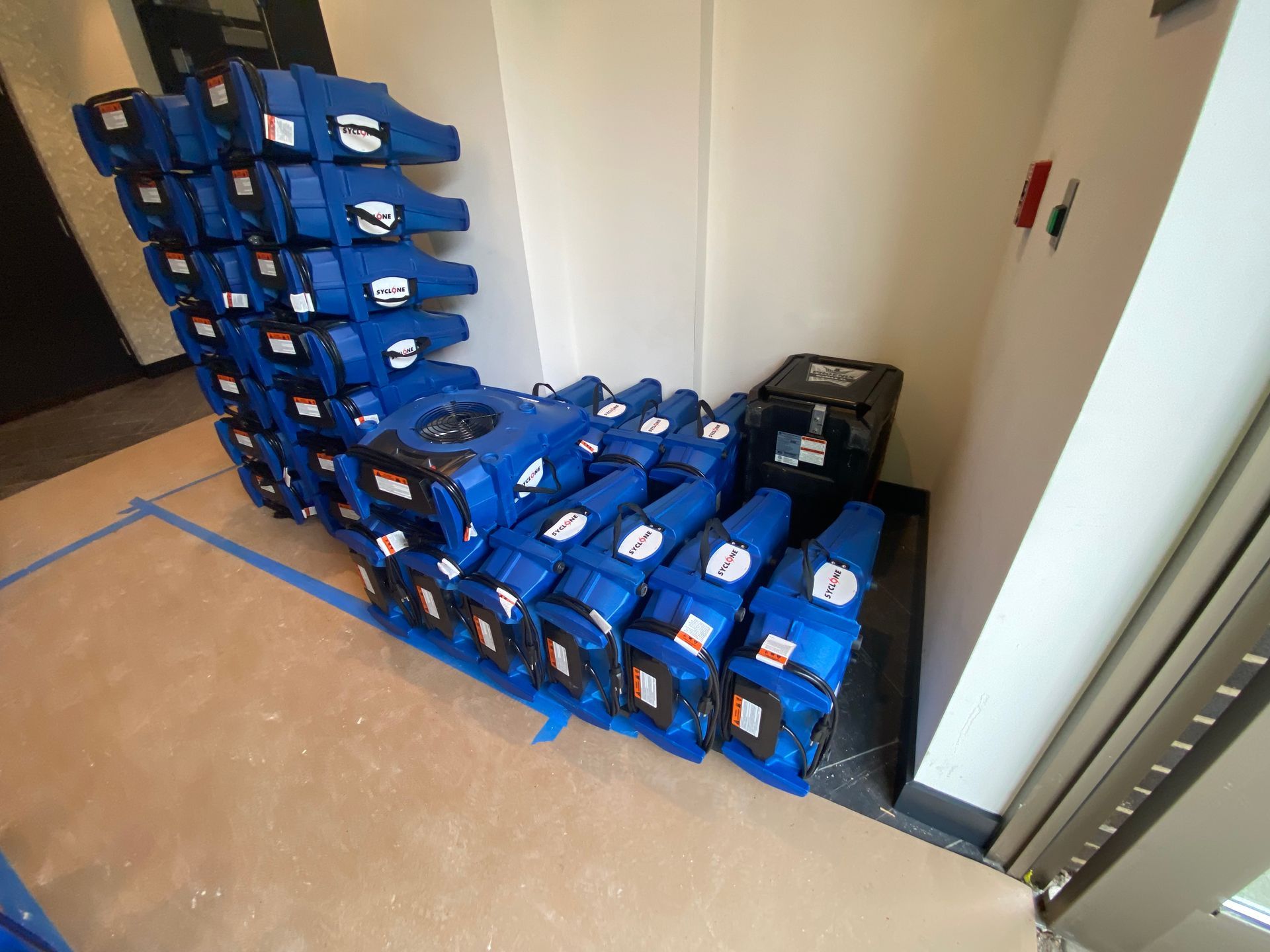Blue air movers stacked in a corner to dry a flooded room.