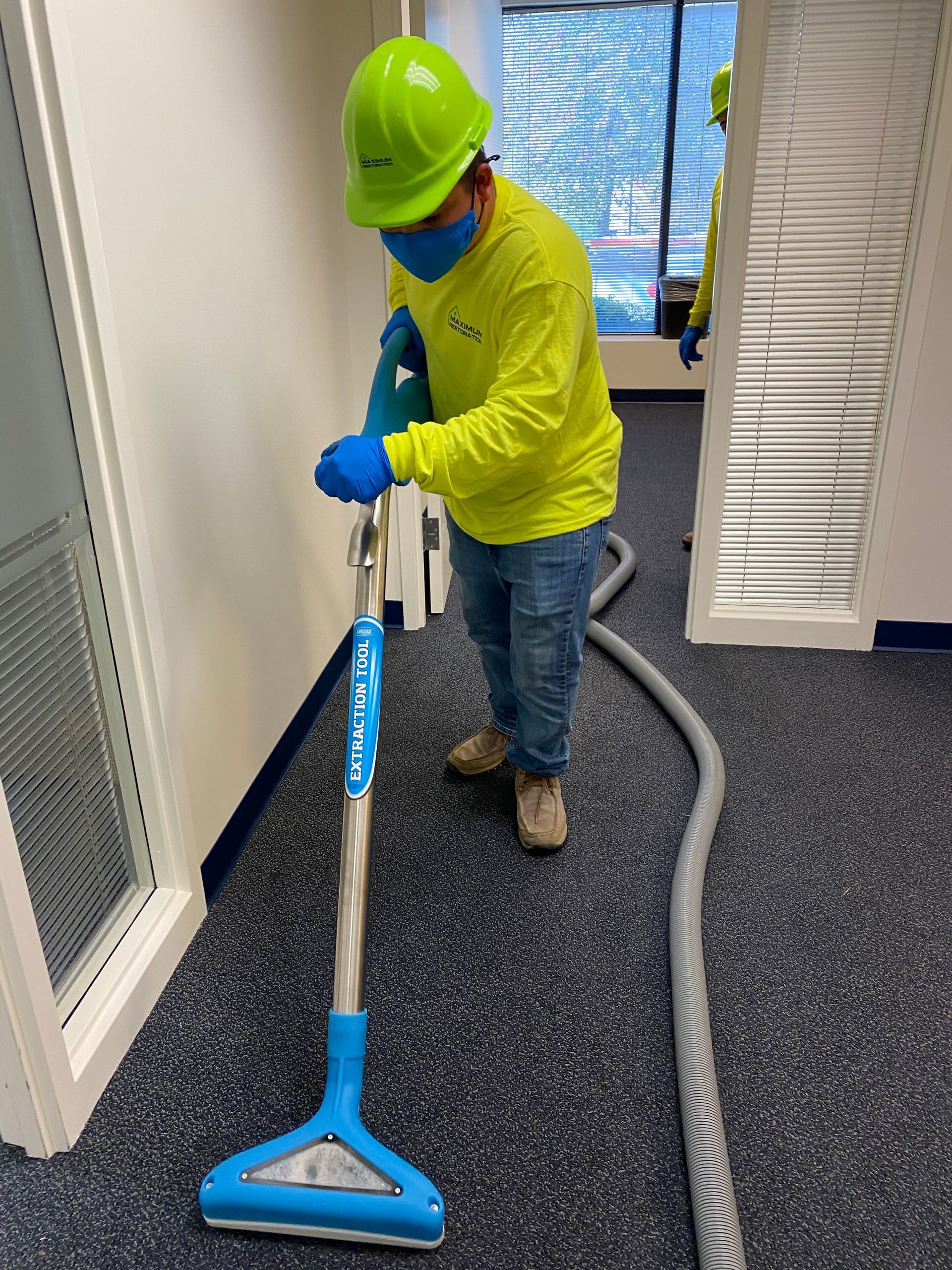 Person in safety gear vacuums a blue carpeted office.