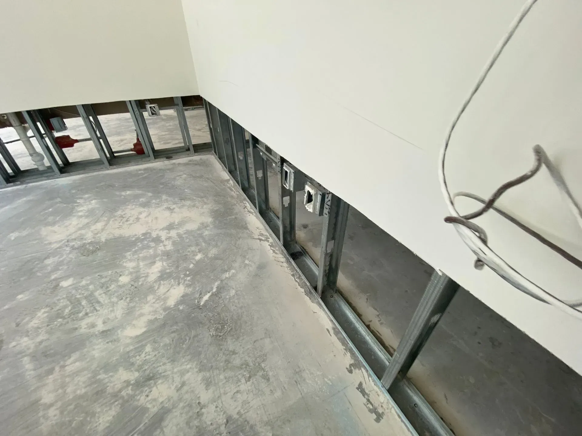 An interior space under renovation with exposed metal wall studs, concrete flooring, and unfinished drywall.
