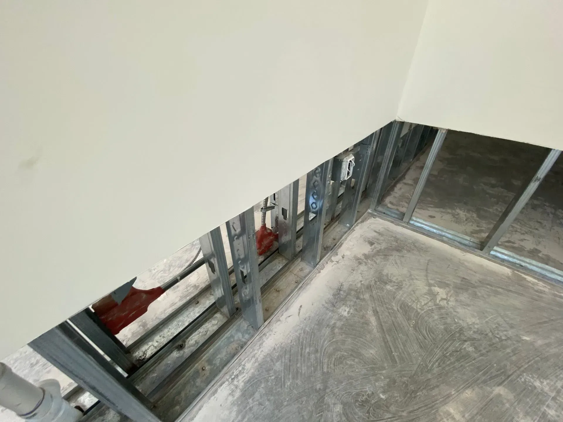 An interior view of unfinished construction showing metal wall studs and exposed electrical wiring along a corner.