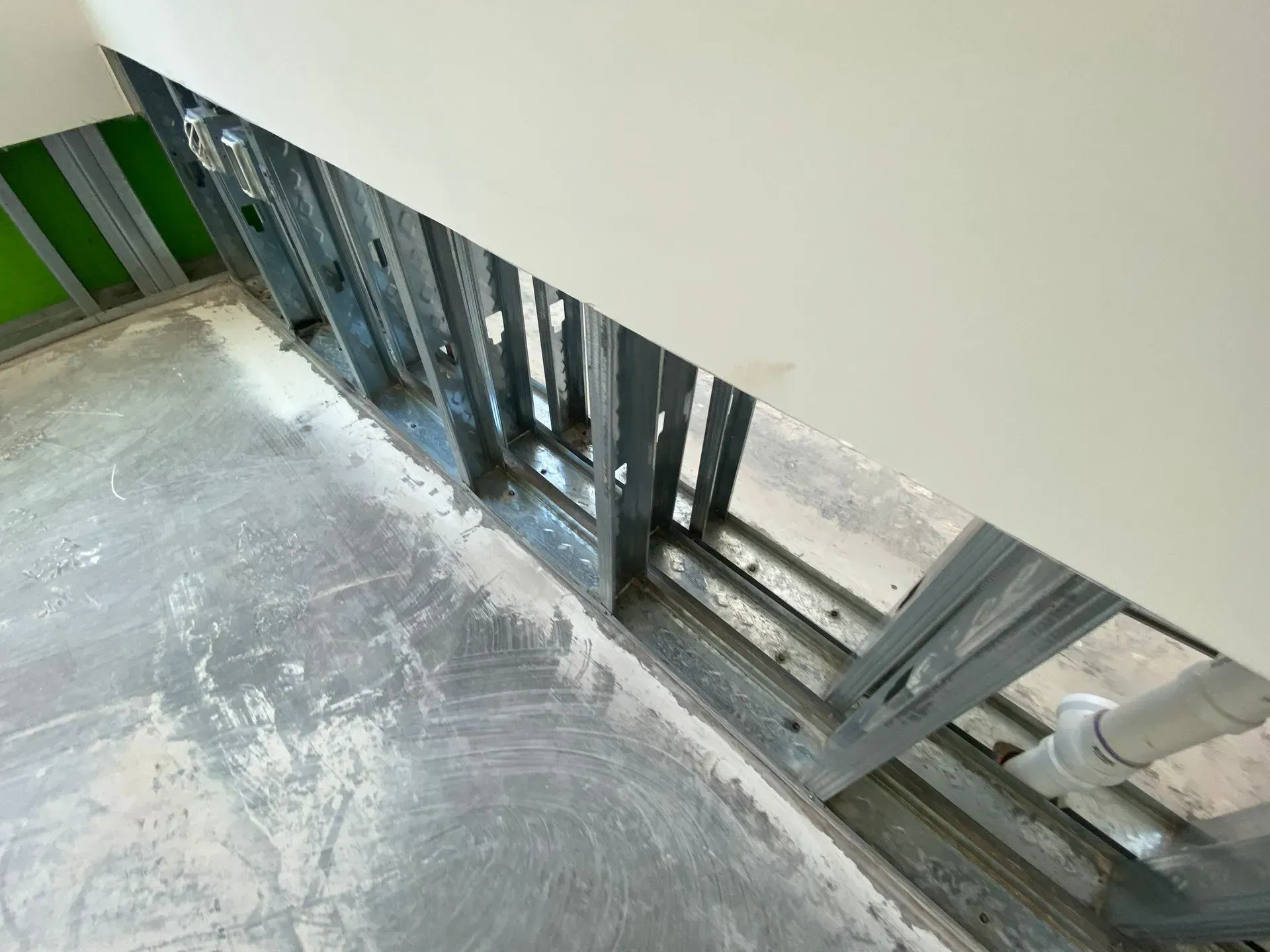 An interior view of a room under construction, showing metal wall studs and a white pipe extending from the concrete floor.
