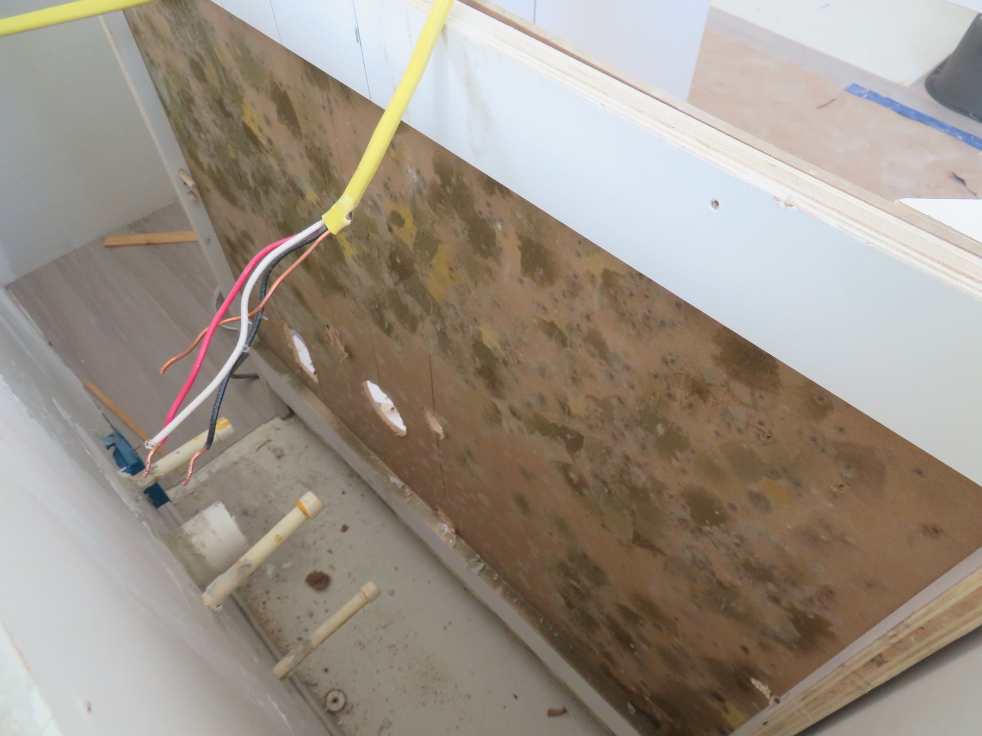 Exposed electrical wires hang in front of a cabinet wall showing signs of dark mold growth in an unfinished room.