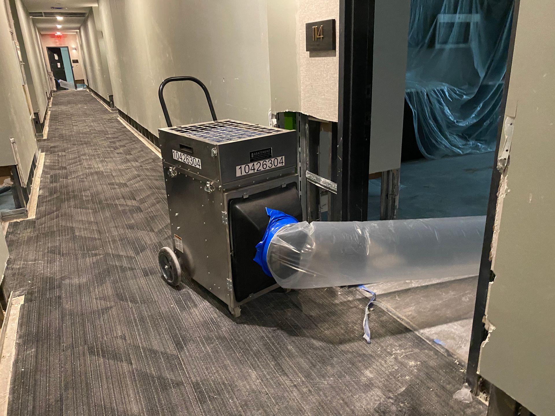 Industrial air scrubber with a duct extending into a hotel room to dry the carpet and area.