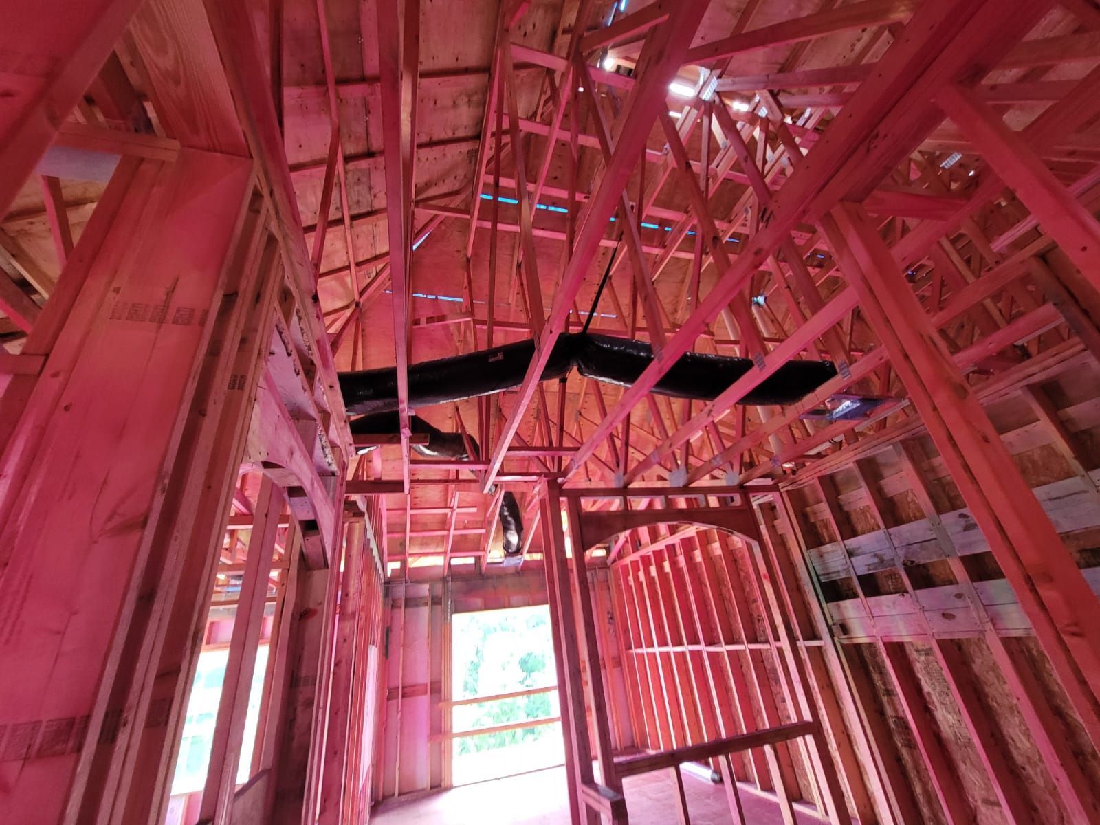 Interior view of a residential building under construction with exposed wooden framing and dark flexible ductwork.