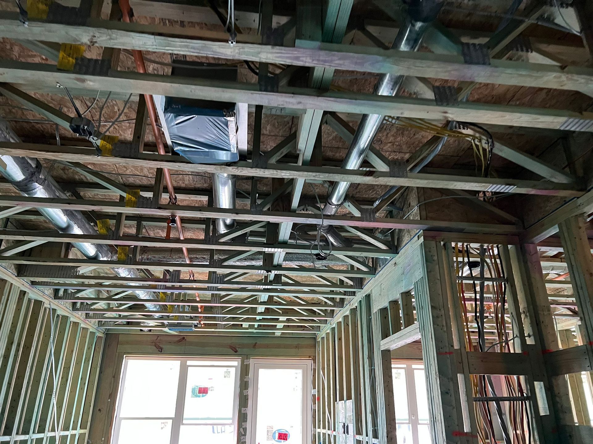 The interior of a building under construction, showing wooden wall studs, ceiling trusses, and installed ductwork.