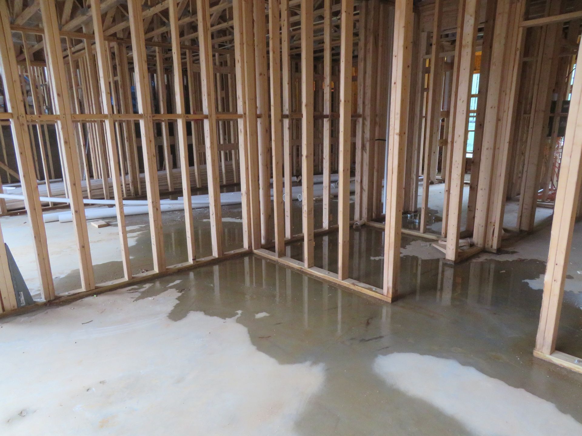 Interior of a building under construction featuring wood wall framing and a concrete floor with areas of standing water.