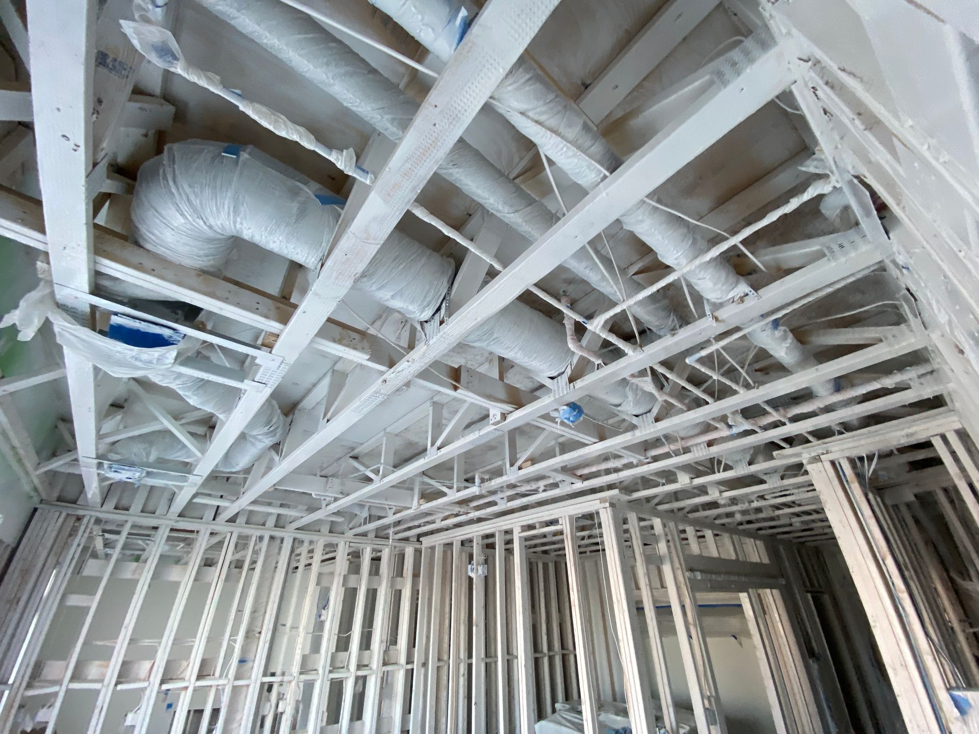 Unfinished room interior featuring light wood wall framing and exposed white ductwork installed in the ceiling joists.