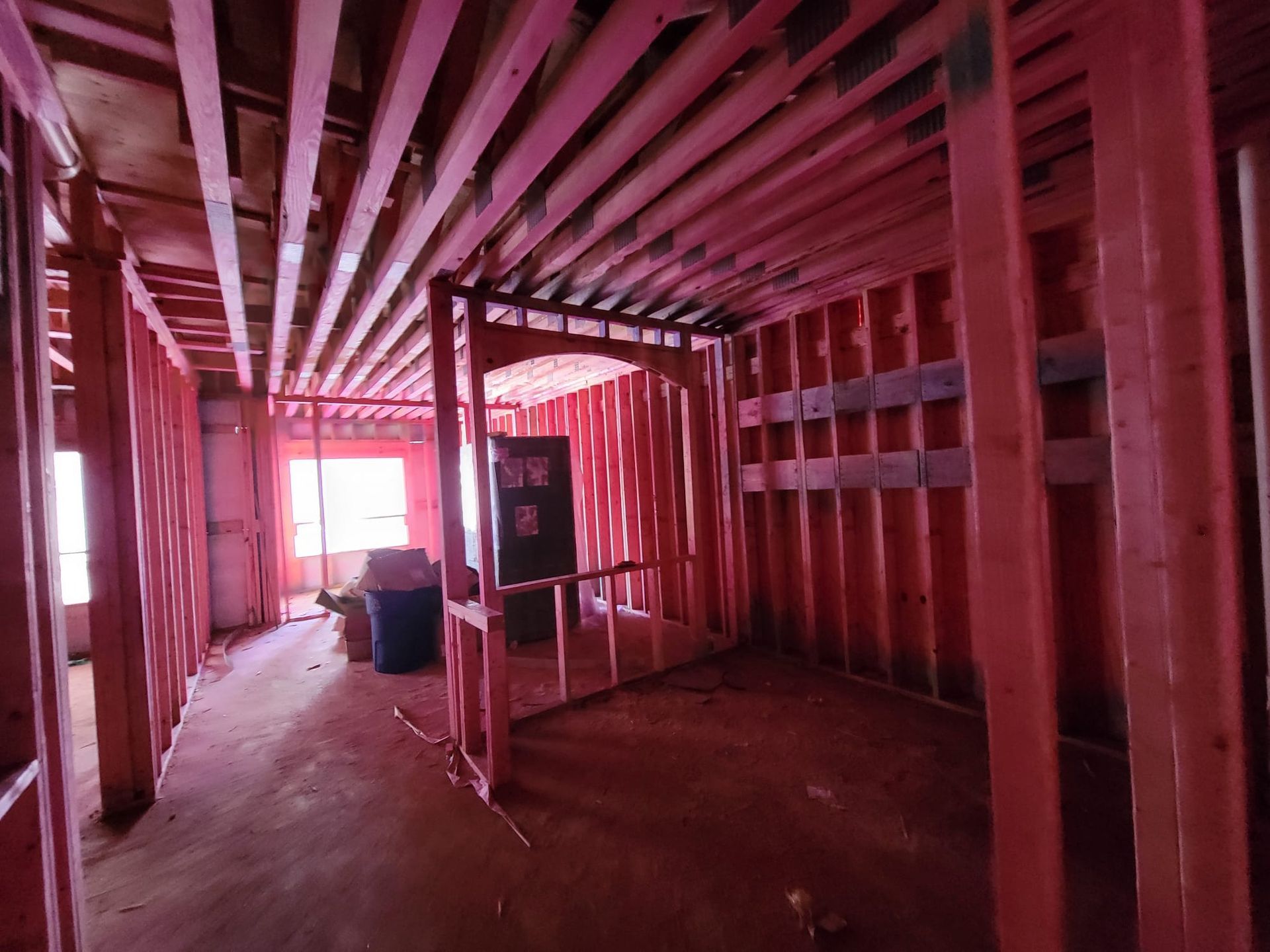 The interior of a building under construction featuring exposed wood framing, studs, and ceiling joists.