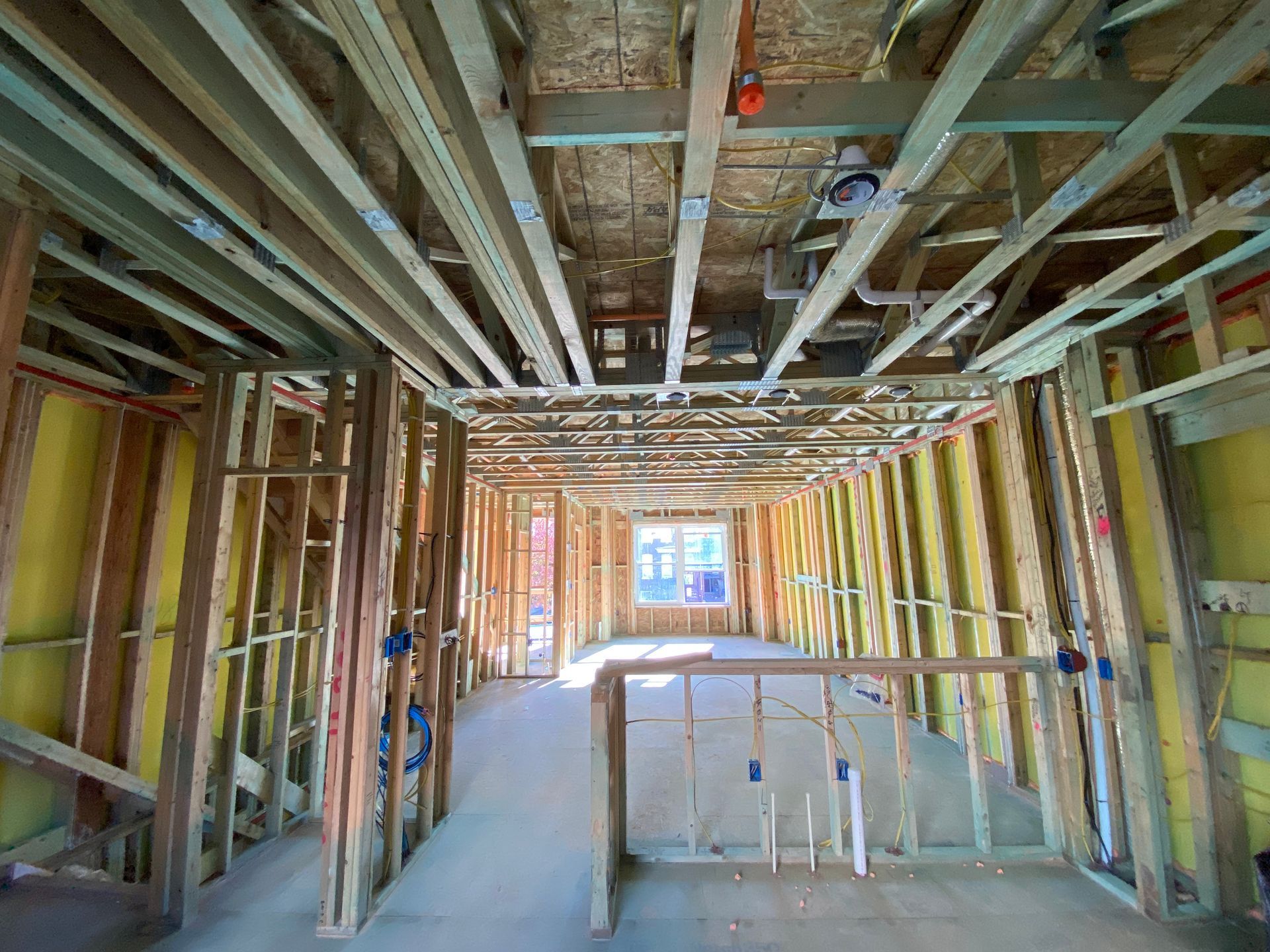 Interior view of an unfinished wood-framed house under construction with exposed beams, wall studs, and insulation.