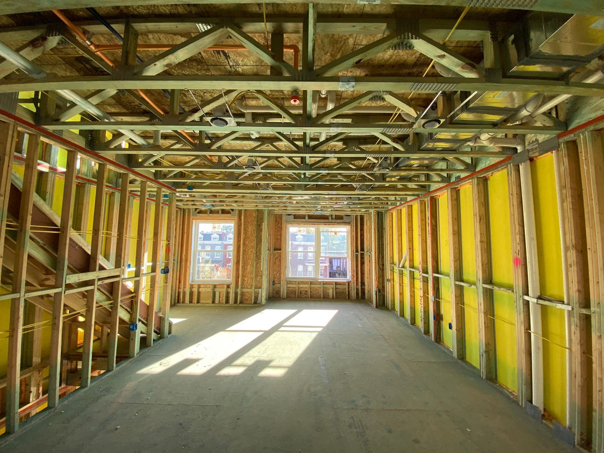 Unfinished interior of a building under construction featuring metal ceiling joists, wood-framed walls, and two windows.