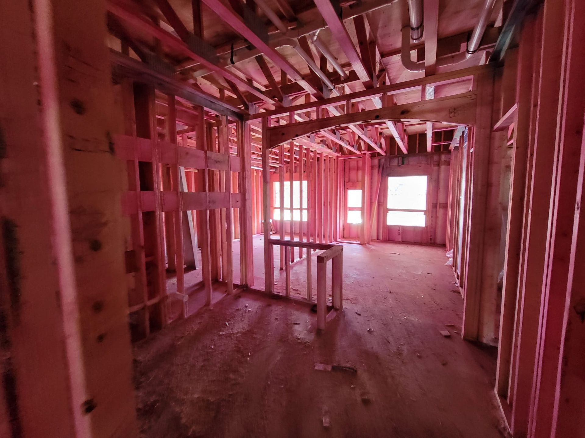 Unfinished house interior with exposed pink framing and wood floor, lit by bright windows.