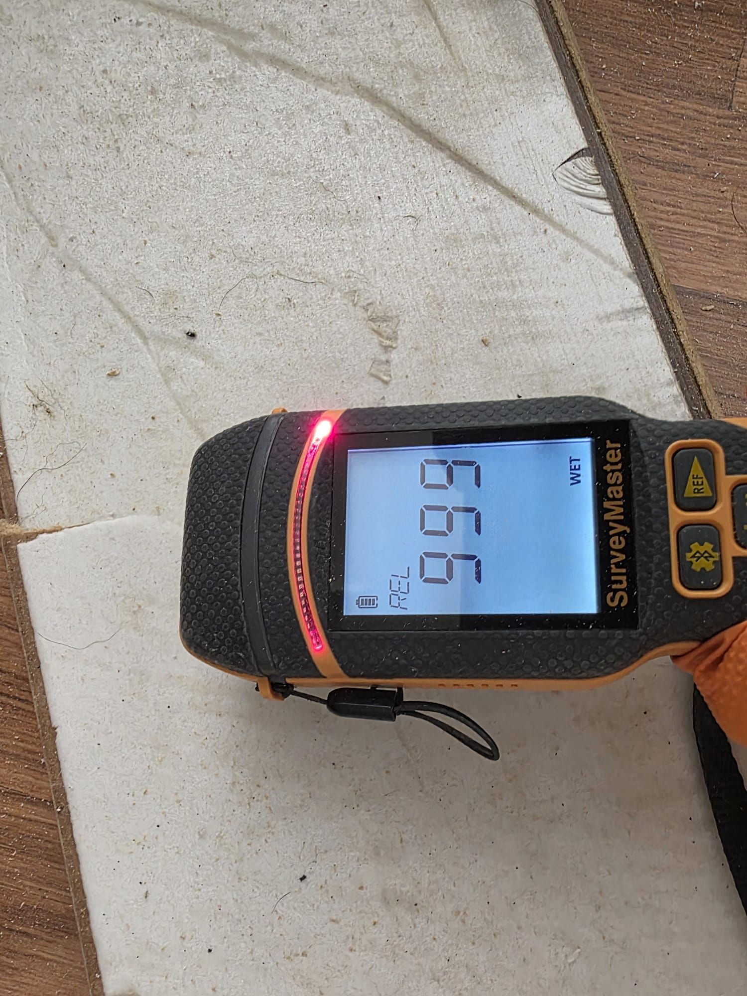 A Protimeter SurveyMaster moisture meter held against a white tile surface, displaying a maximum reading of 999.