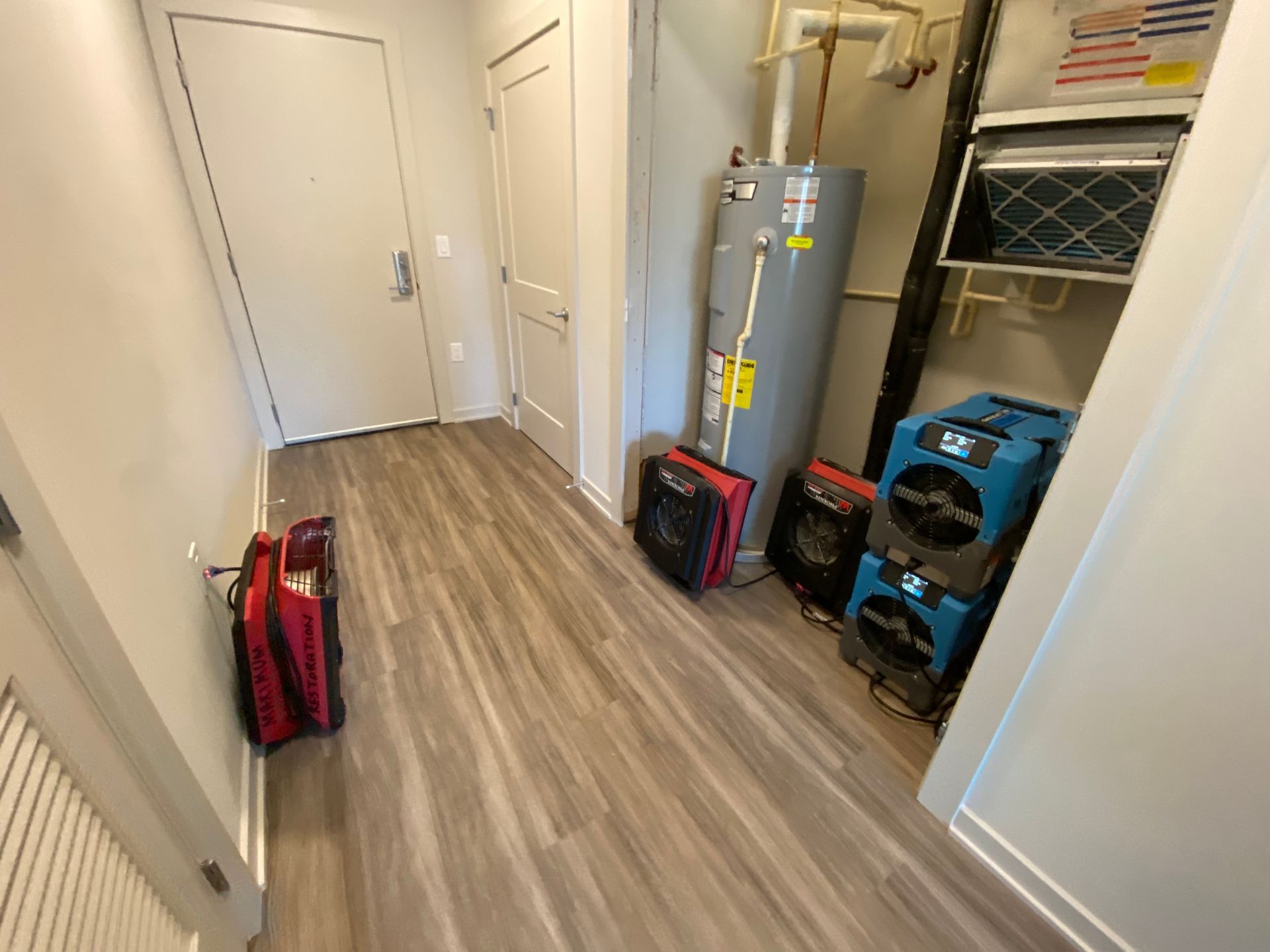 A hallway contains a water heater, HVAC equipment, and several red and blue industrial drying fans for water restoration.