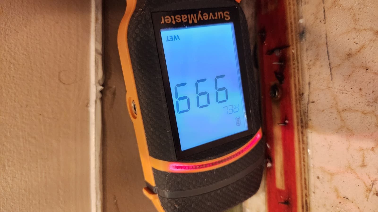 A Protimeter SurveyMaster moisture meter held against a wall, displaying a 