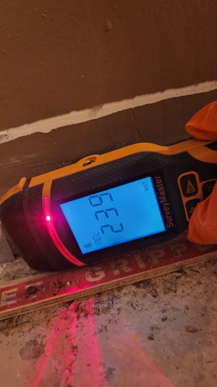 A Protimeter SurveyMaster tool displaying a reading of 23.9 on a blue screen while held against a floor surface.