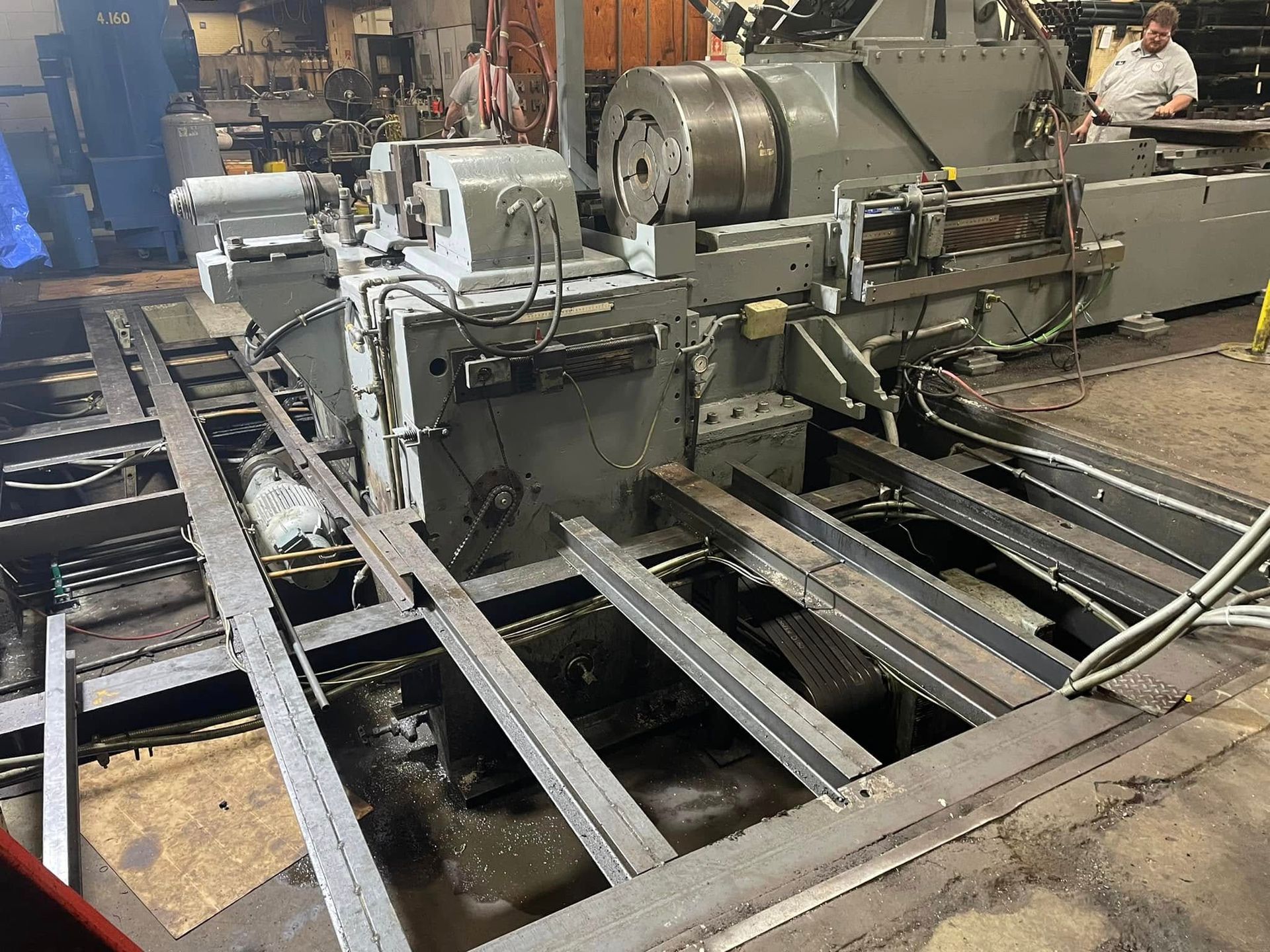Industrial machine in a workshop, with metal rails and a worker in the background.
