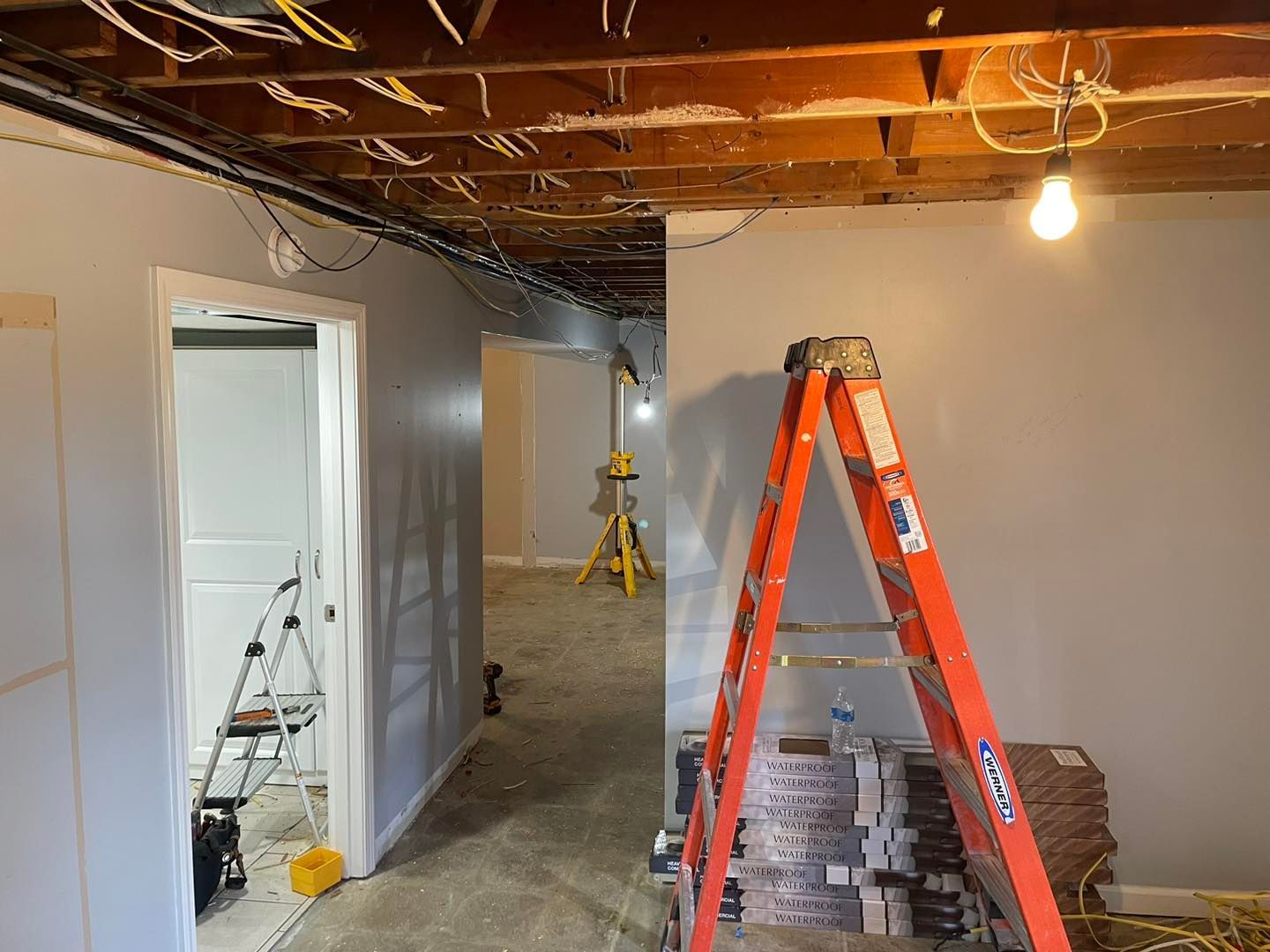 Basement under renovation with ladders, exposed ceiling joists, and construction materials.