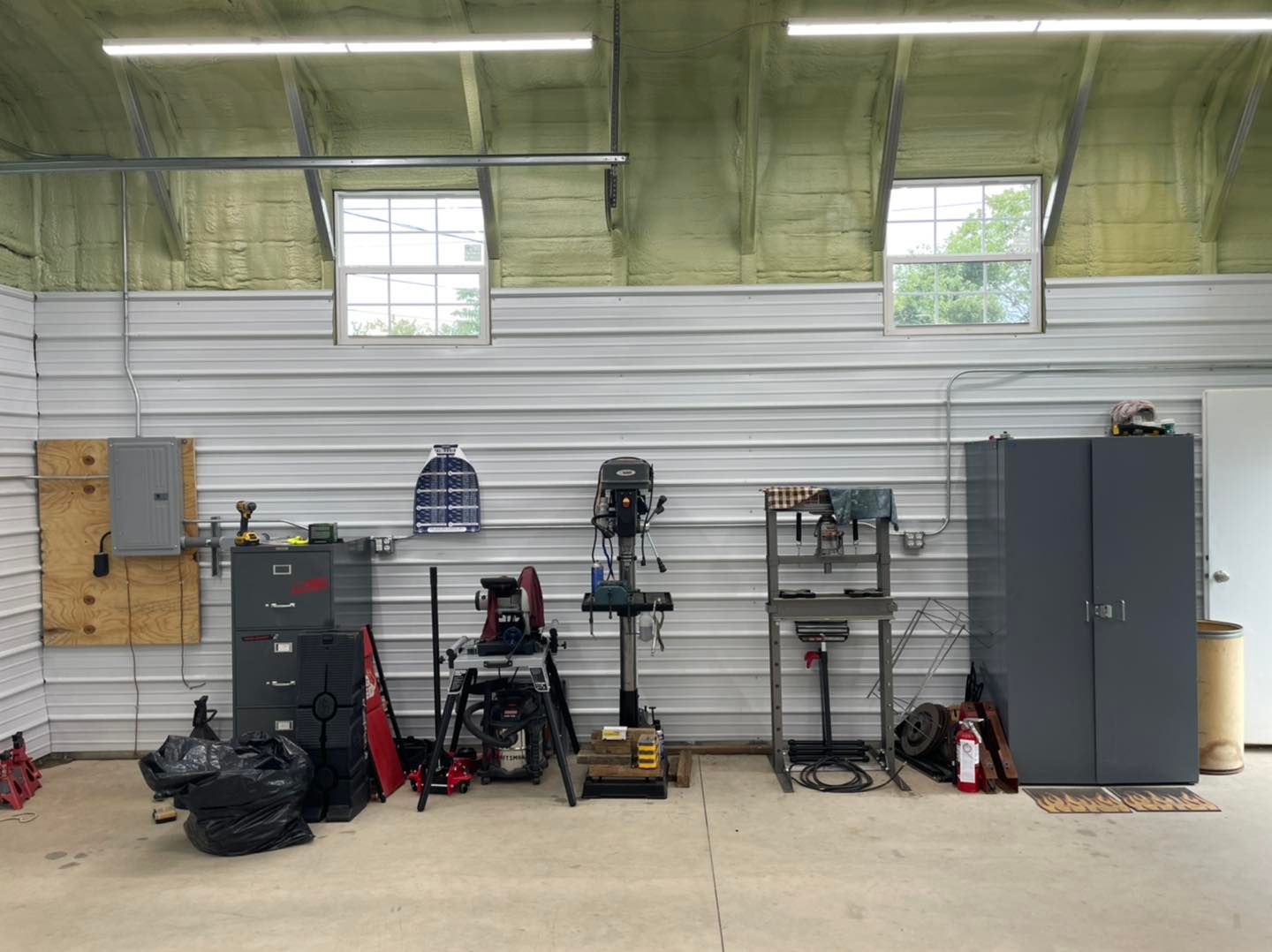 Workshop wall with shelves, tools, cabinets, and a gray storage locker under high windows