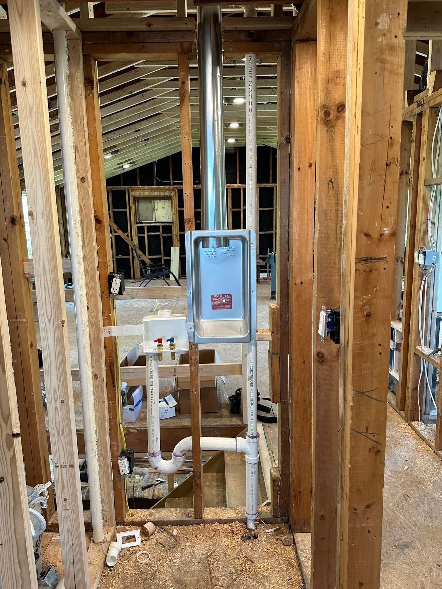 Interior wall framing under construction with exposed wood studs, pipes, and a blue electrical panel.