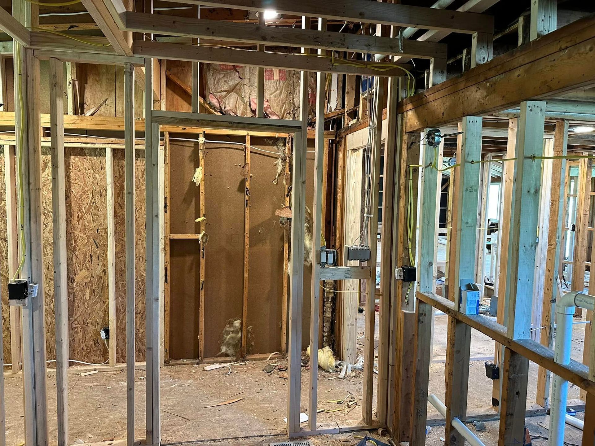Framed interior under construction with exposed wood studs, insulation, and unfinished doorway.
