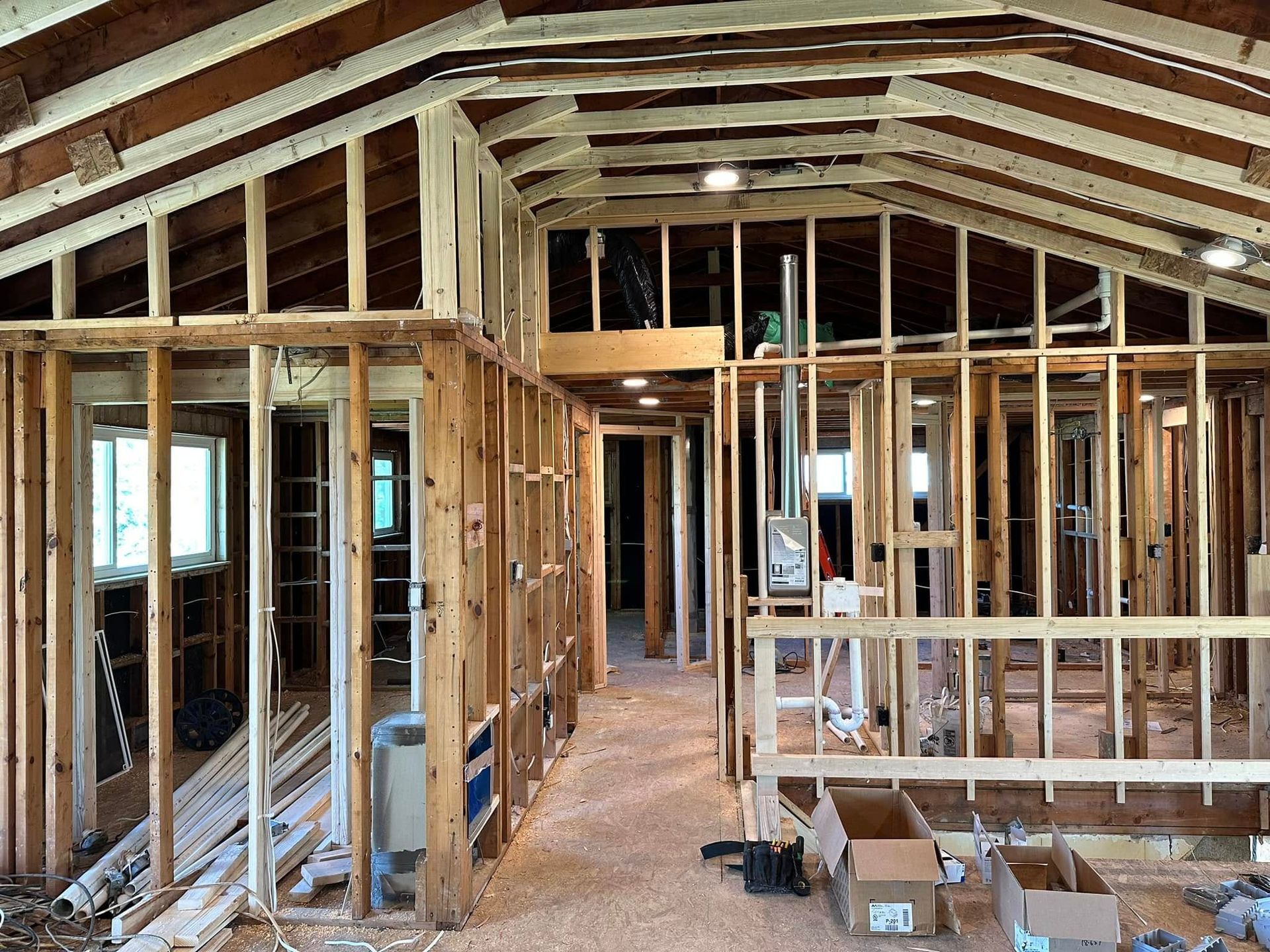 Unfinished house interior with exposed wood framing, open ceiling beams, and construction materials on the floor