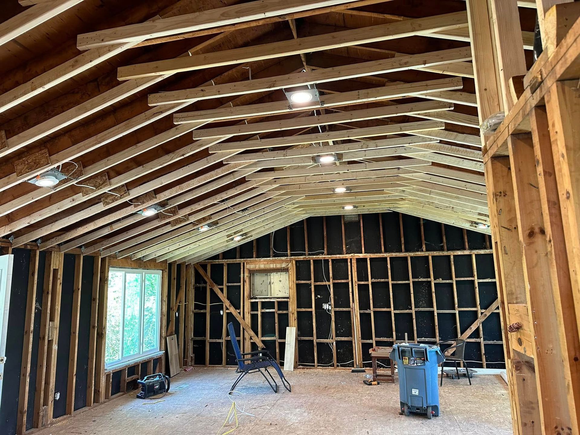 Unfinished attic with exposed wooden framing, insulation, and construction tools on the floor.
