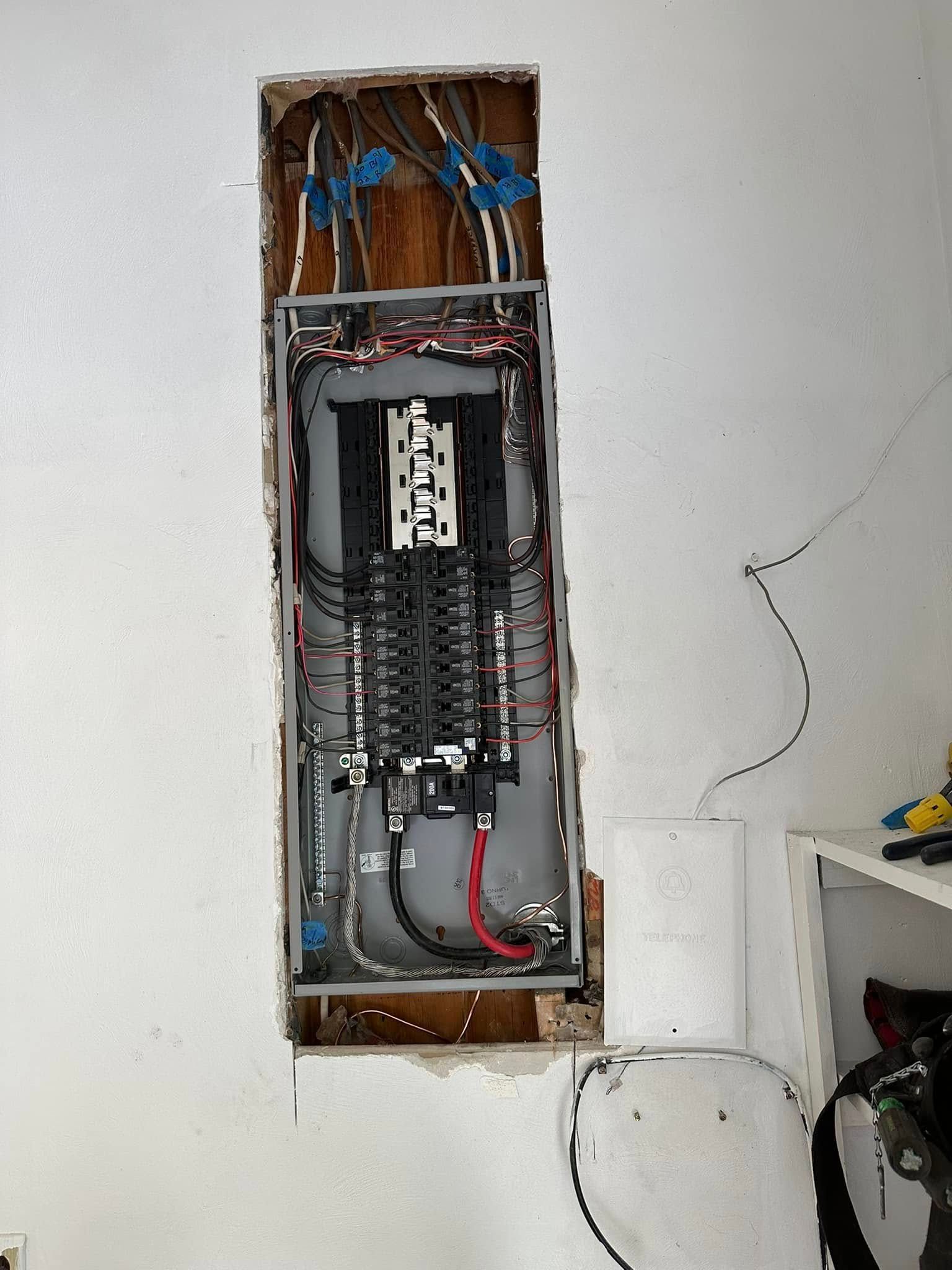 Open electrical breaker panel exposed in a wall cavity with visible wiring and cables.