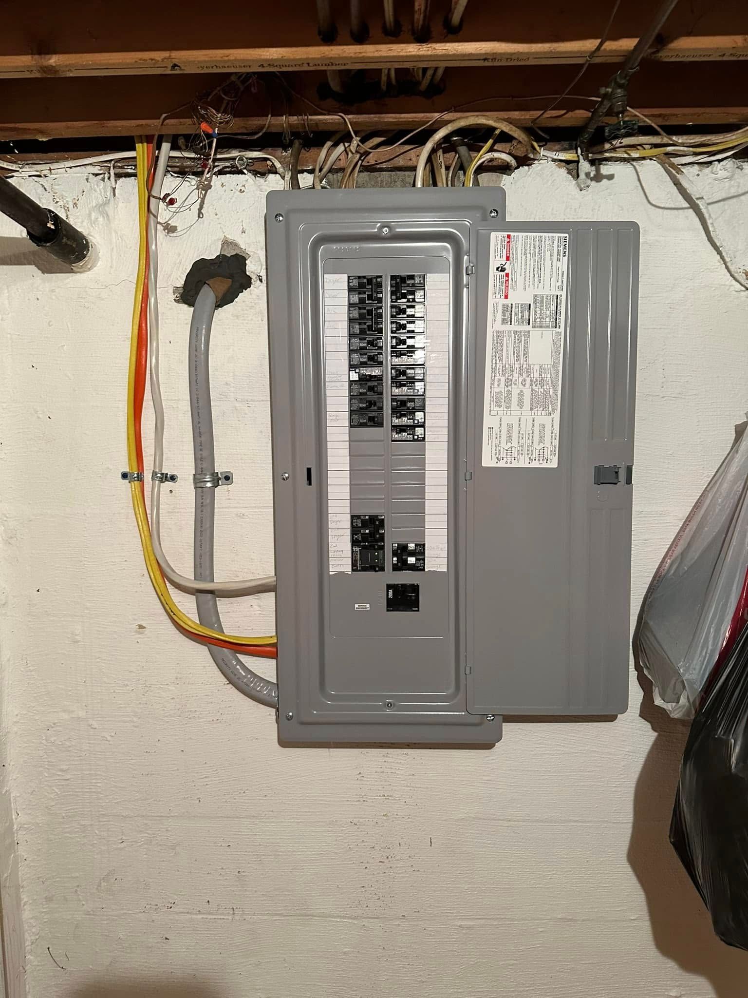 Gray electrical breaker panel on a basement wall with exposed wiring overhead.
